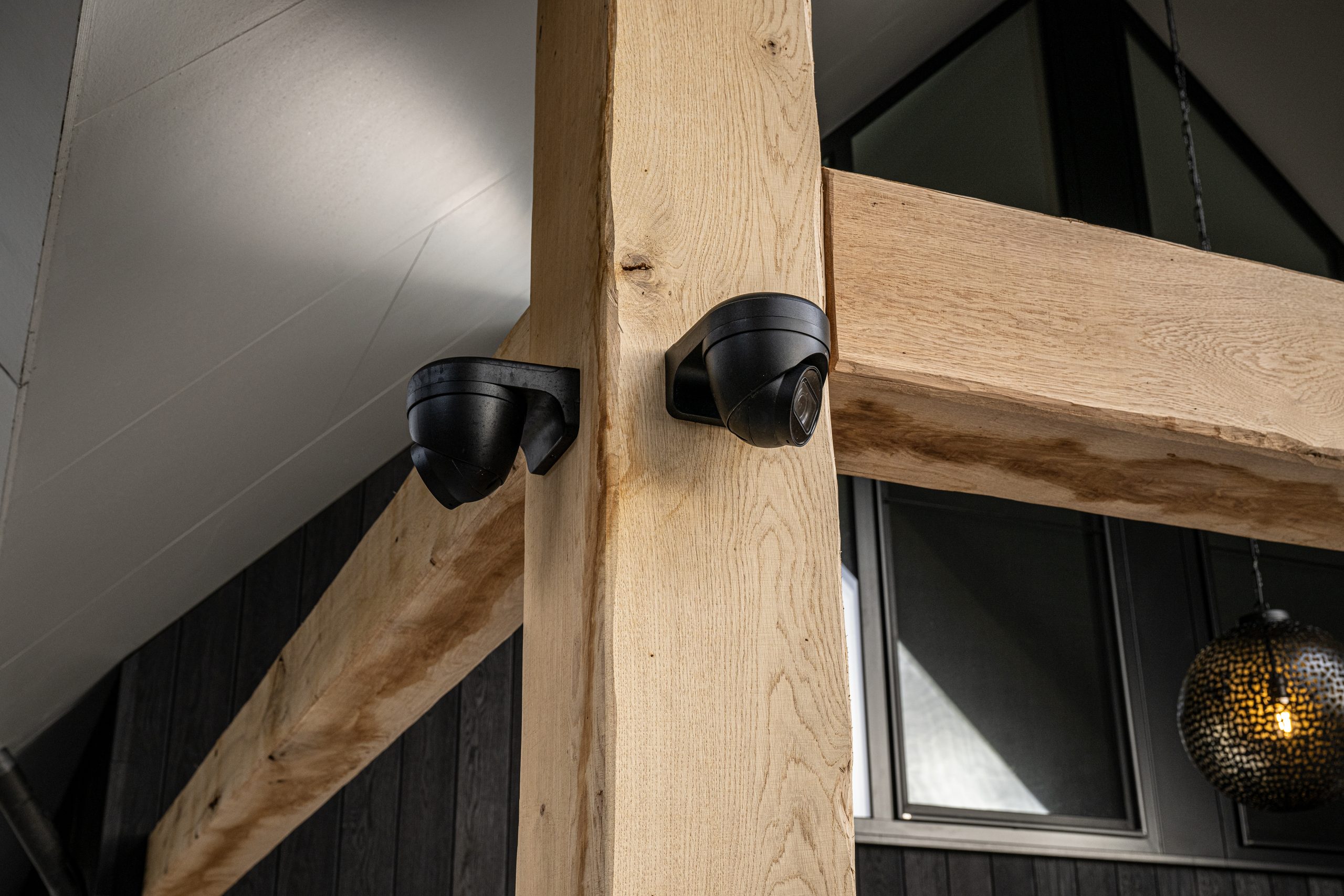 Detailopname van beveiligingscamera's die naadloos zijn verwerkt in de eikenhouten balkomtimmering van een overkapping.