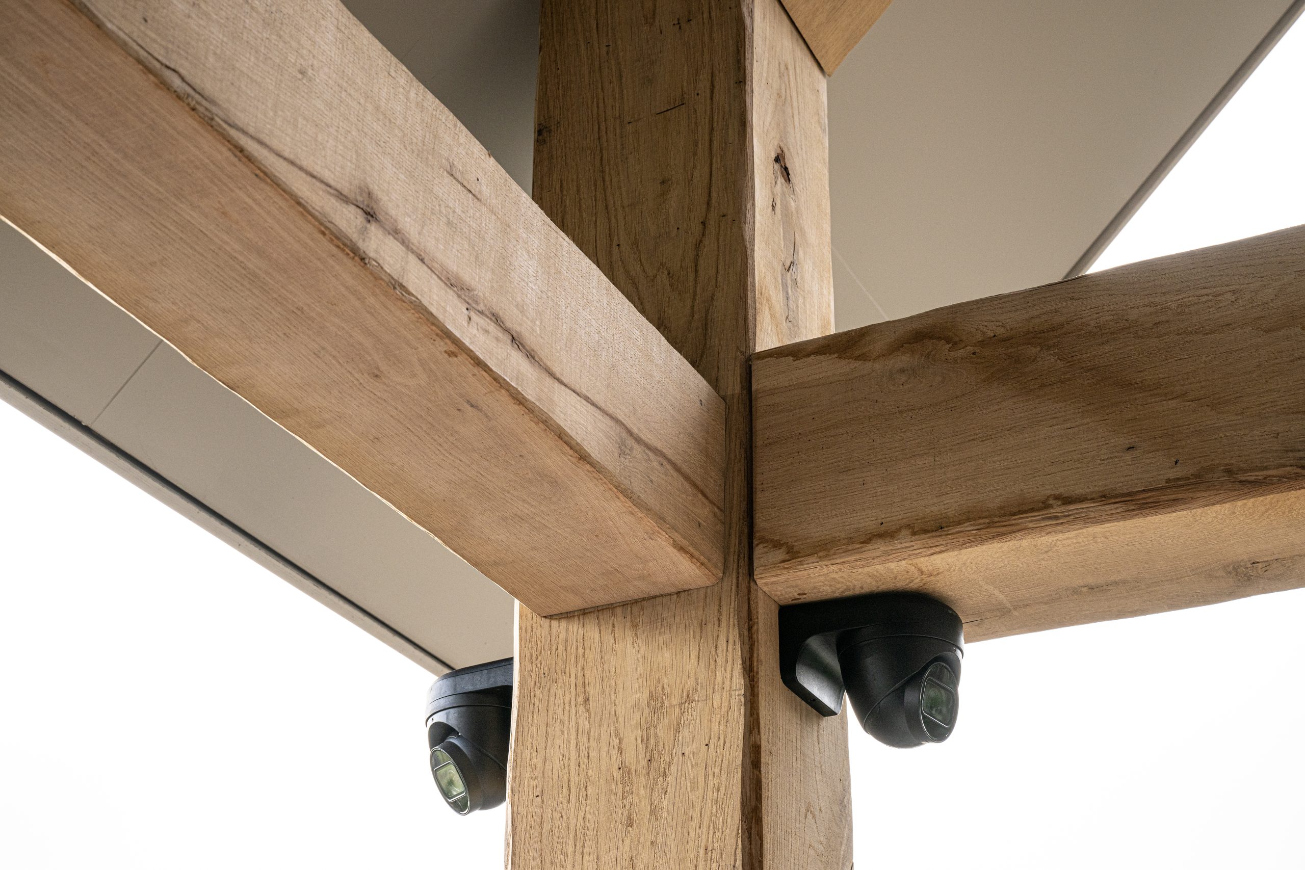Detail van een hoekverbinding van eikenhouten balkomtimmering met gemonteerde zwarte beveiligingscamera's voor woningbeveiliging.