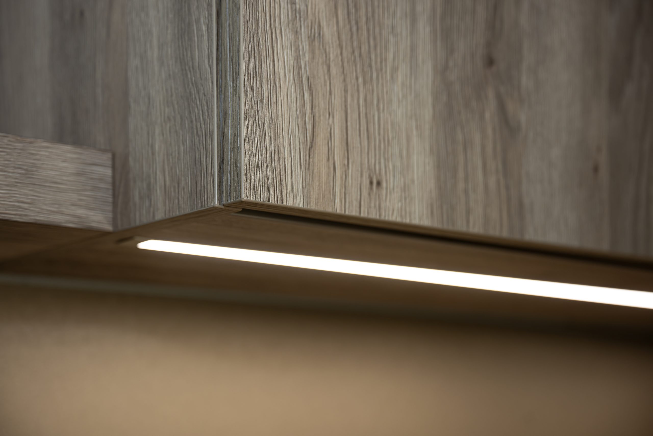 Close-up van de onderzijde van een houten keukenkast met een strak weggewerkte LED-strip voor werkbladverlichting.