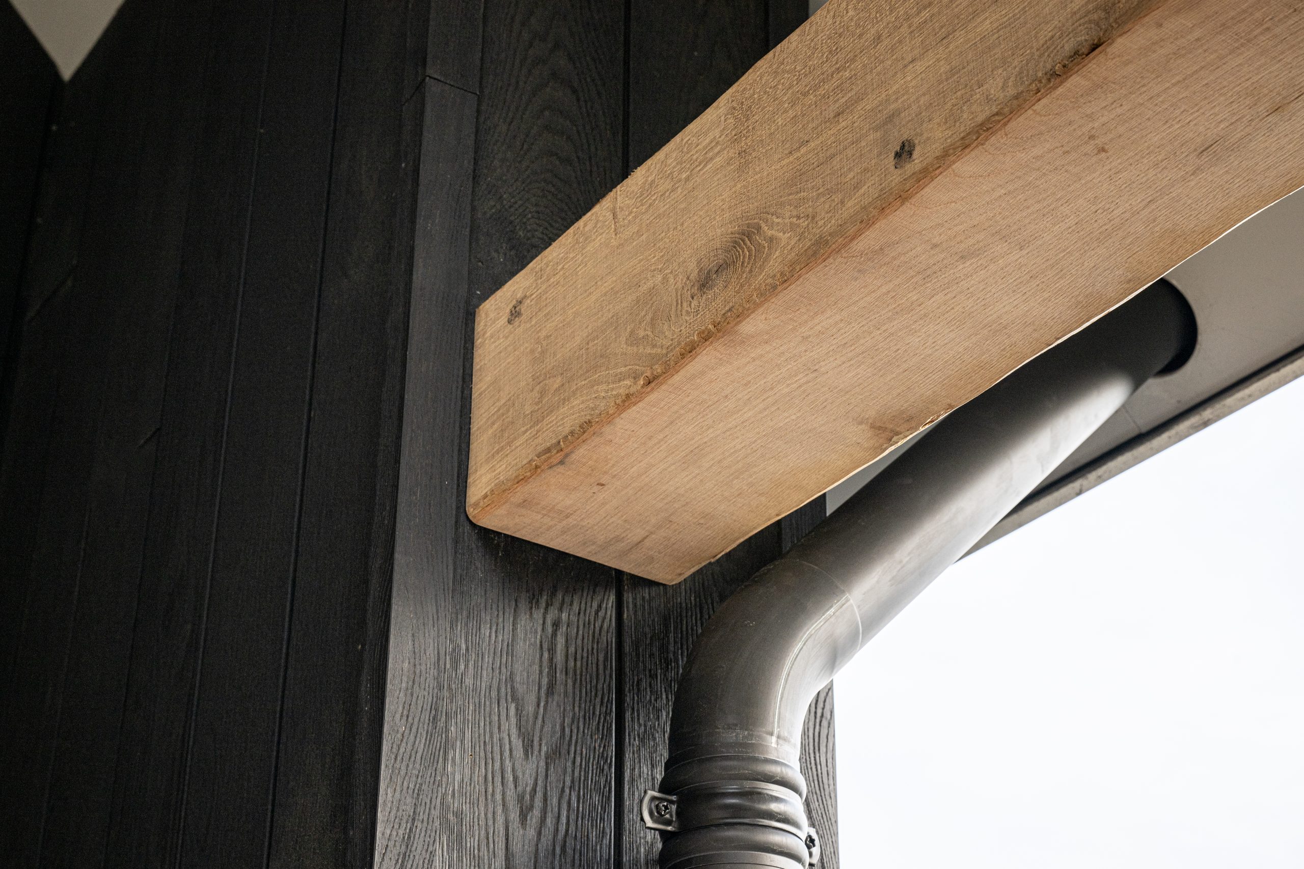 Detail van een horizontale eikenhouten balk die perfect aansluit op de verticale zwarte houten gevelbekleding.