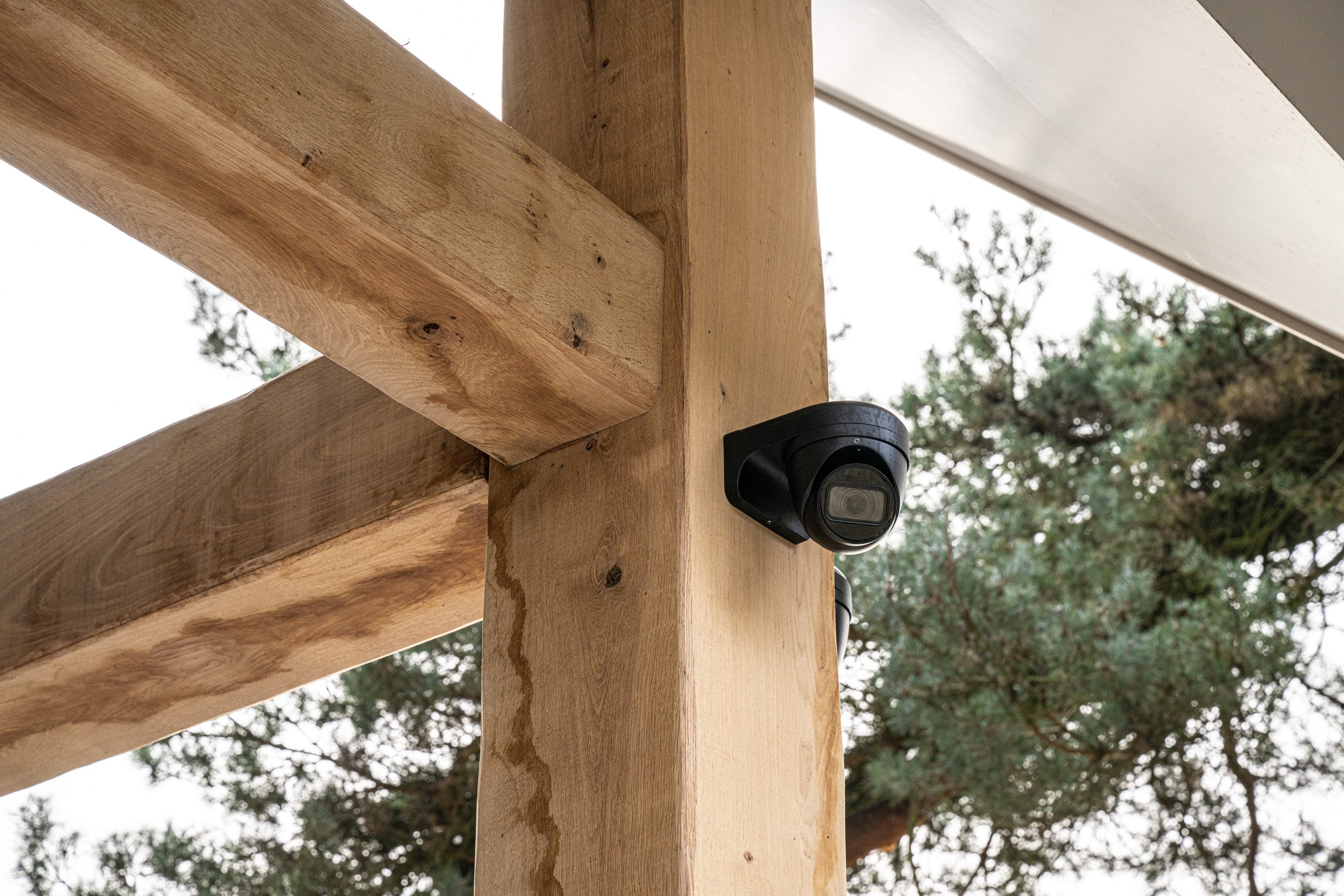 Een eikenhouten balk die een stalen drager bekleedt, voorzien van een zwarte camera met uitzicht op de tuin.
