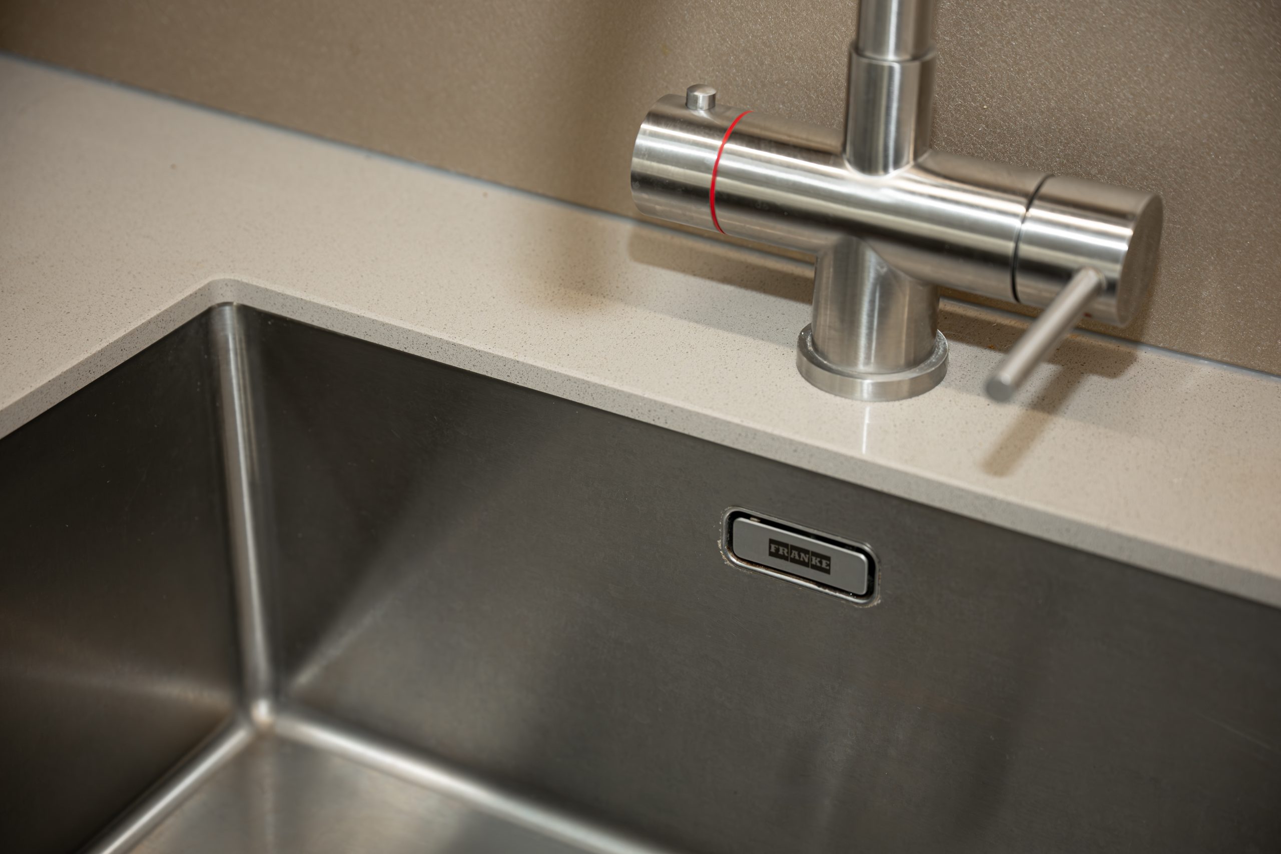 Close-up van een Franke roestvrijstalen spoelbak gemonteerd onder een composiet werkblad met een bijpassende RVS mengkraan.