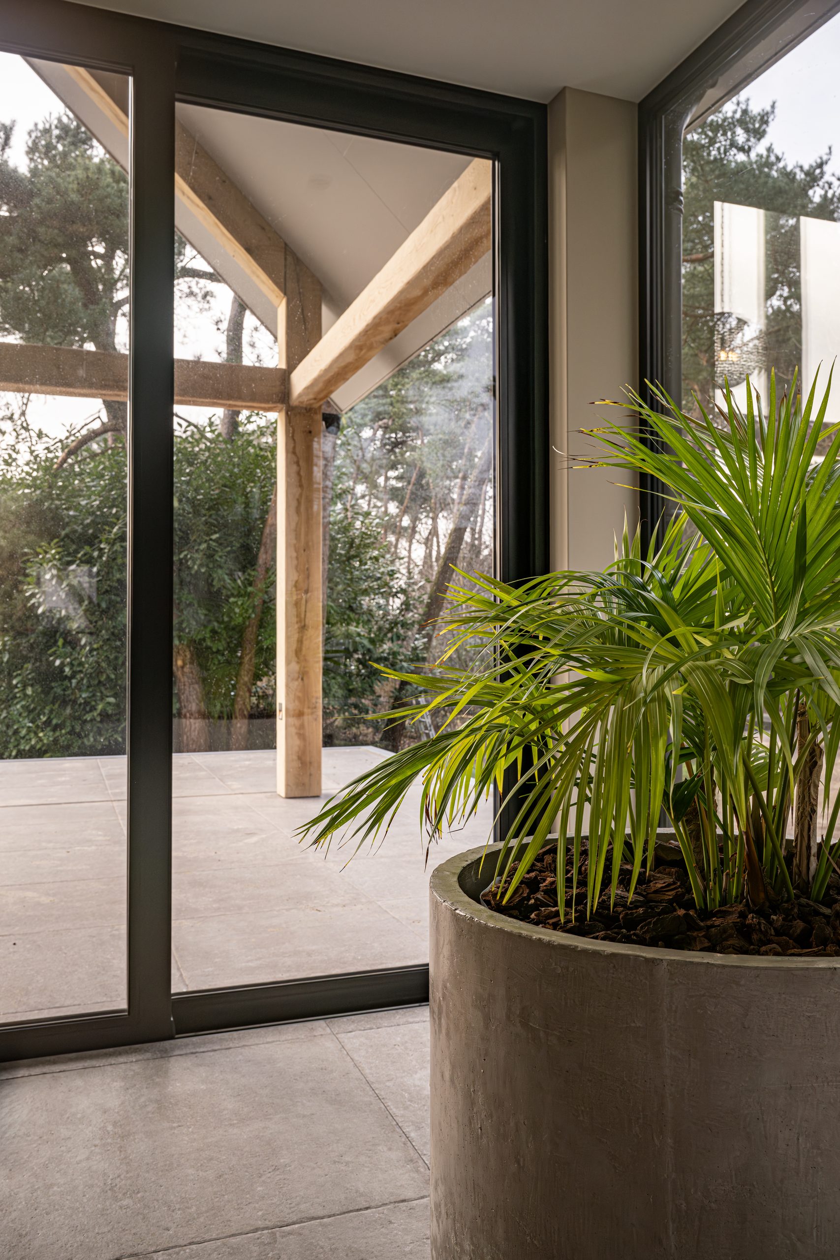 Uitzicht van binnenuit door een grote glazen schuifpui op de eikenhouten balkconstructie van het terras.