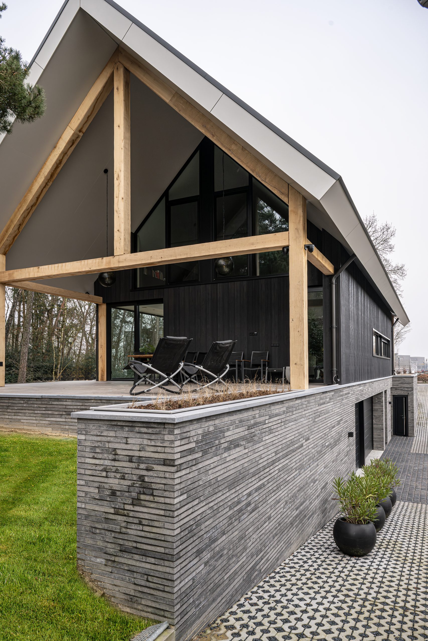 Hoogwaardig terras met een moderne stenen border, eikenhouten balkomtimmeringen en uitzicht op de tuin.