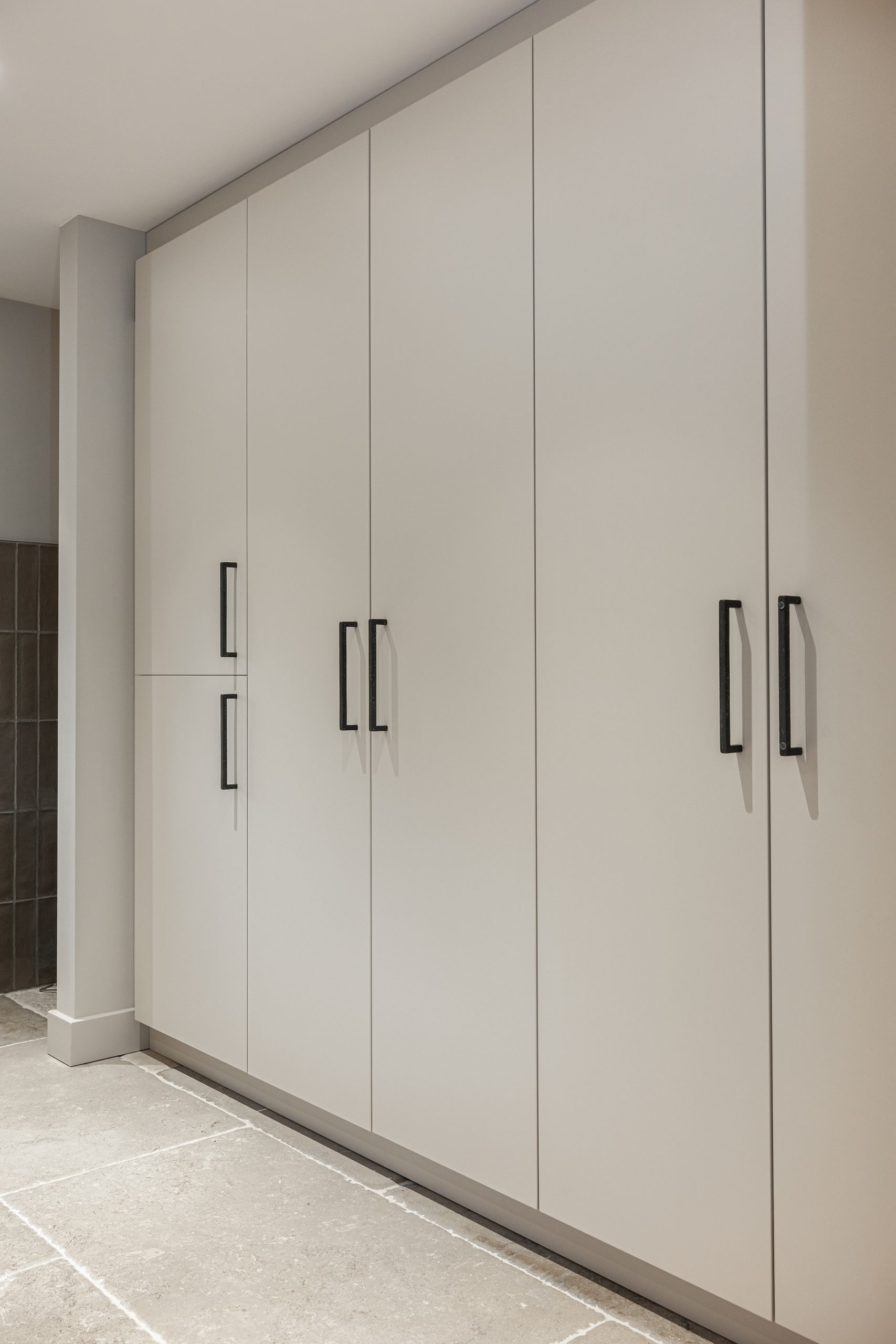 Strakke, plafondhoge maatwerk inbouwkasten in een lichte tint, afgewerkt met verfijnde, lange zwarte handgrepen.