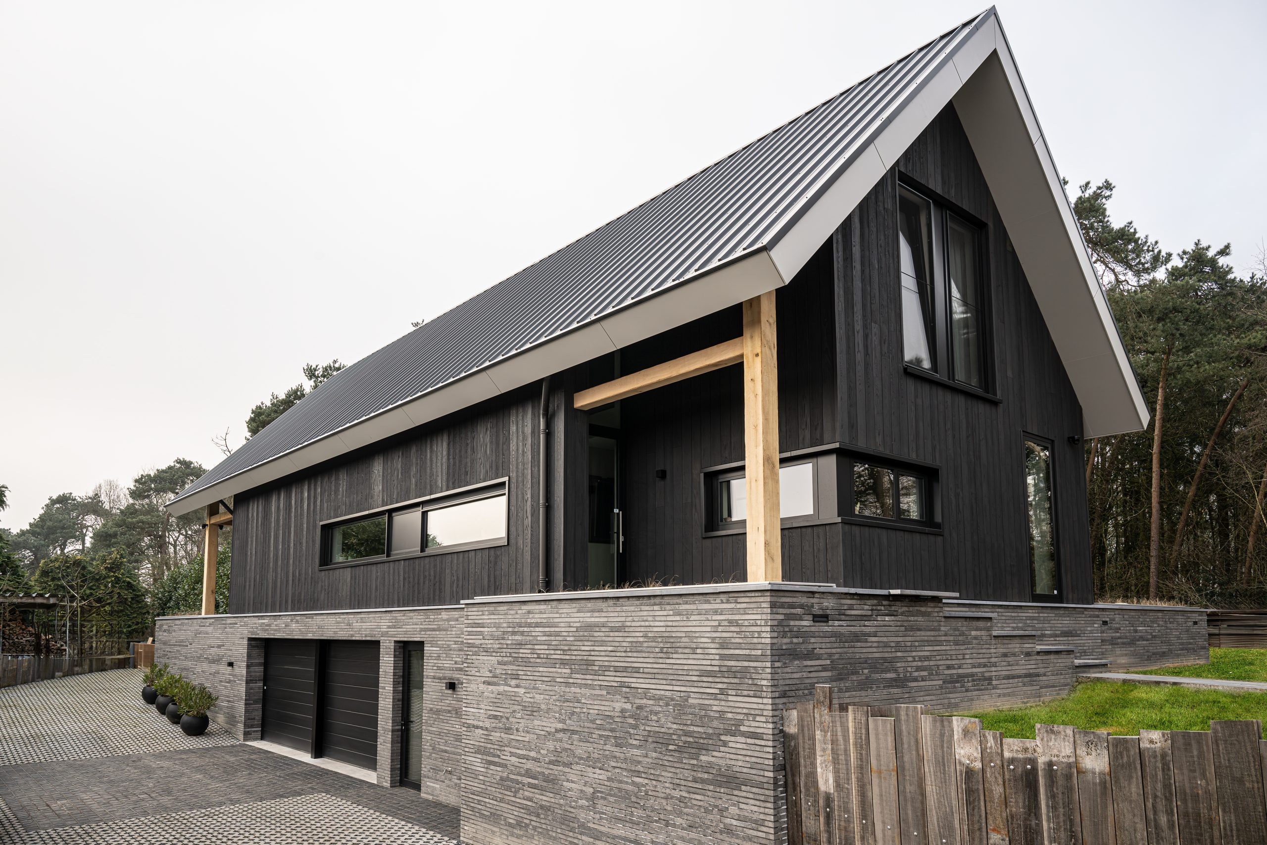 Moderne woning met verticale zwarte gevelbekleding, een grijze bakstenen plint en een eikenhouten kolom bij de entree.