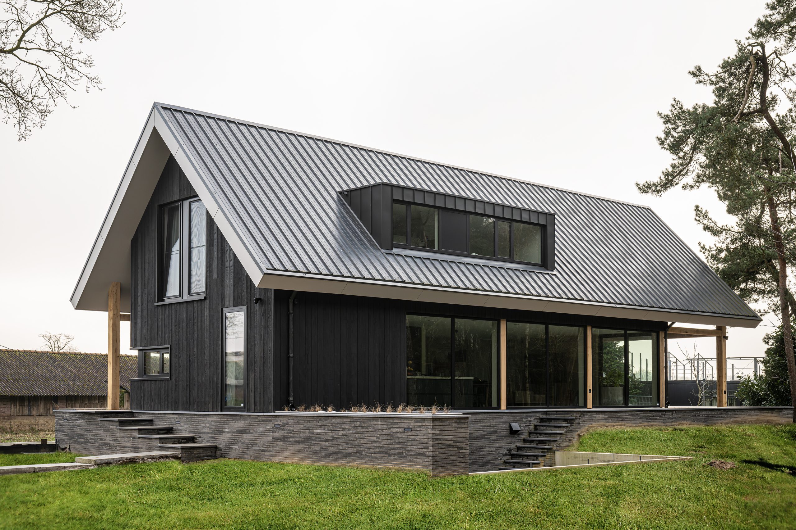 Achteraanzicht van een moderne villa met zwart houten gevels, eikenhouten accenten en een verdiepte oprit naar de garage.