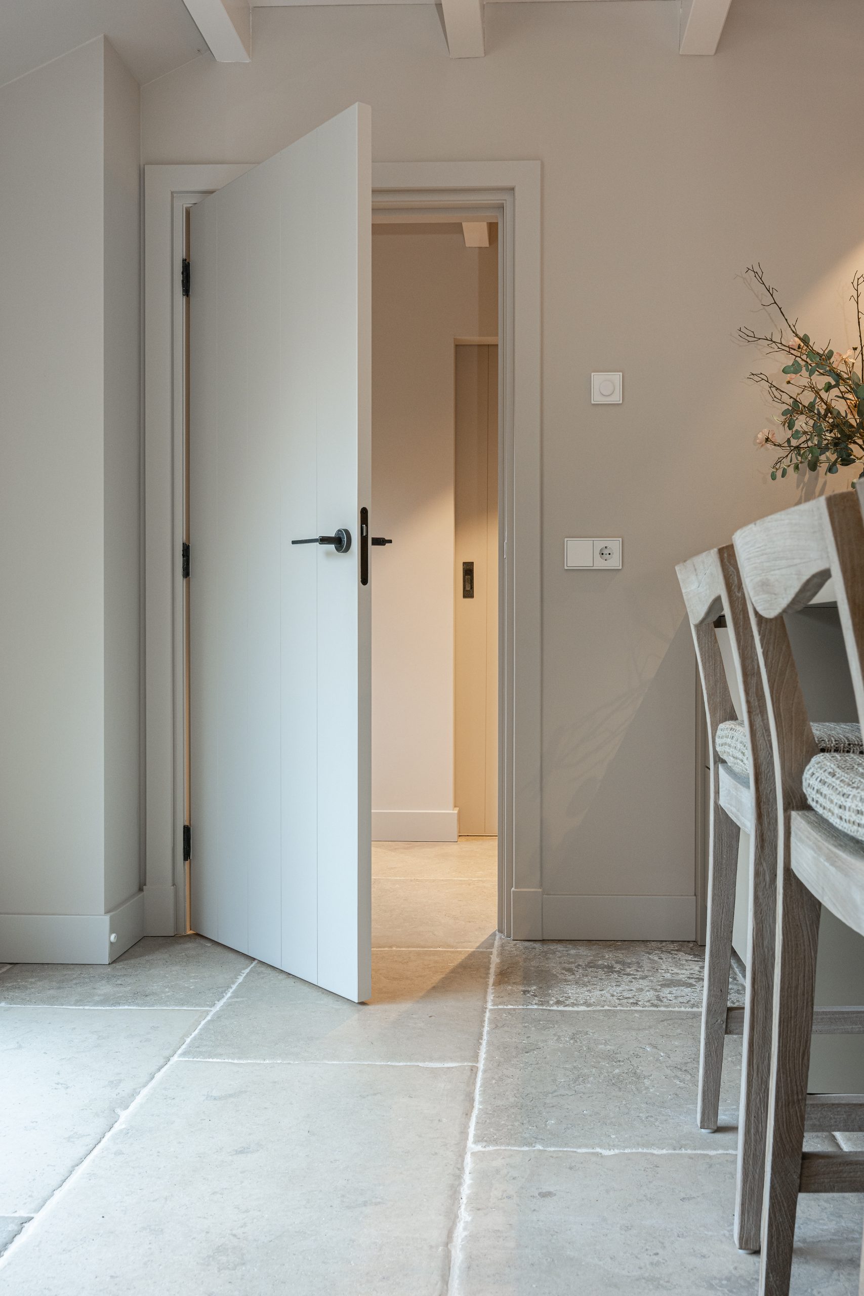 Half geopende witte binnendeur in een landelijk modern interieur, met zicht op de achterliggende hal en lichtinval.