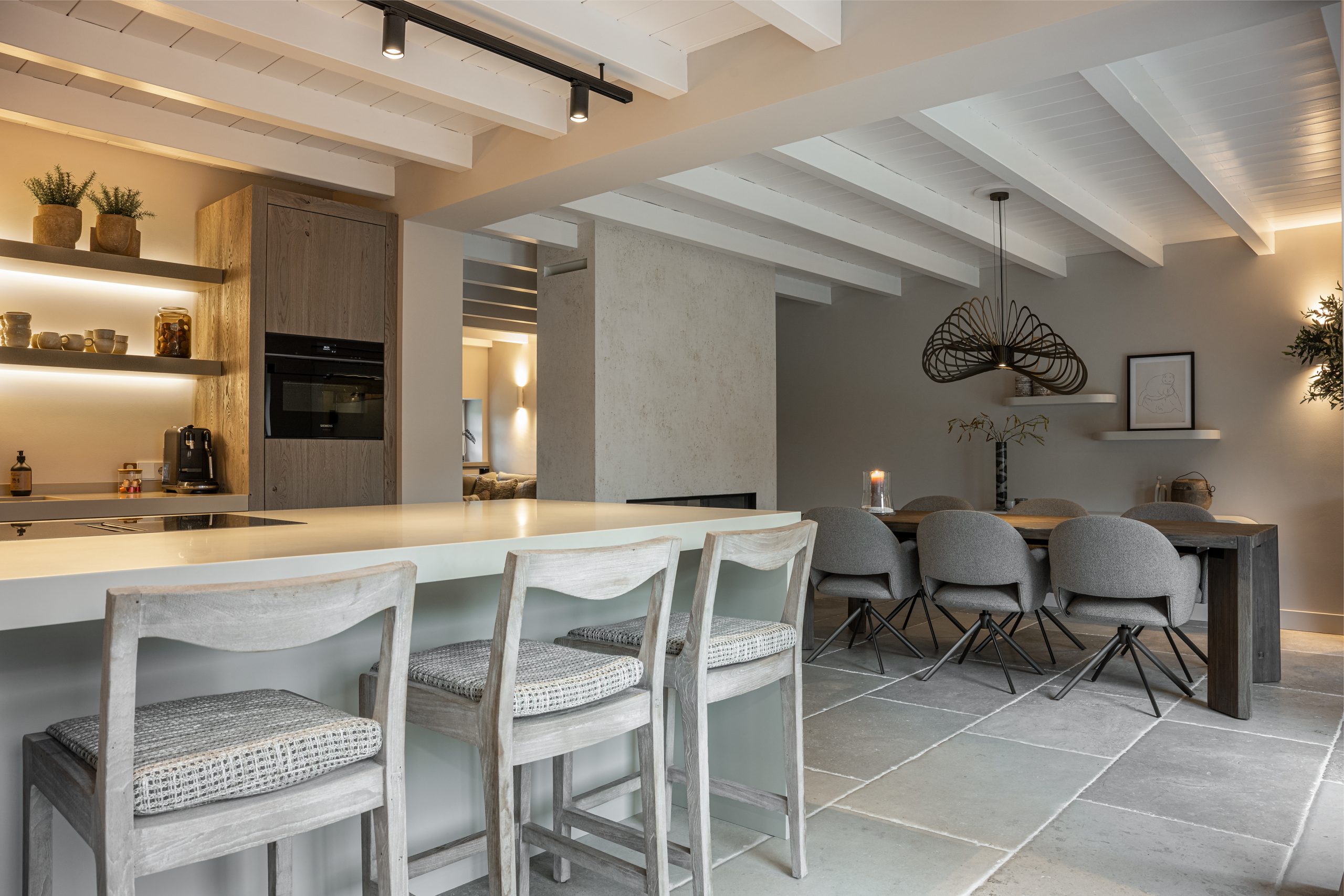 Ruimtelijke woonkeuken met zicht op het kookeiland en de aangrenzende eethoek met grote tafel en design hanglamp.