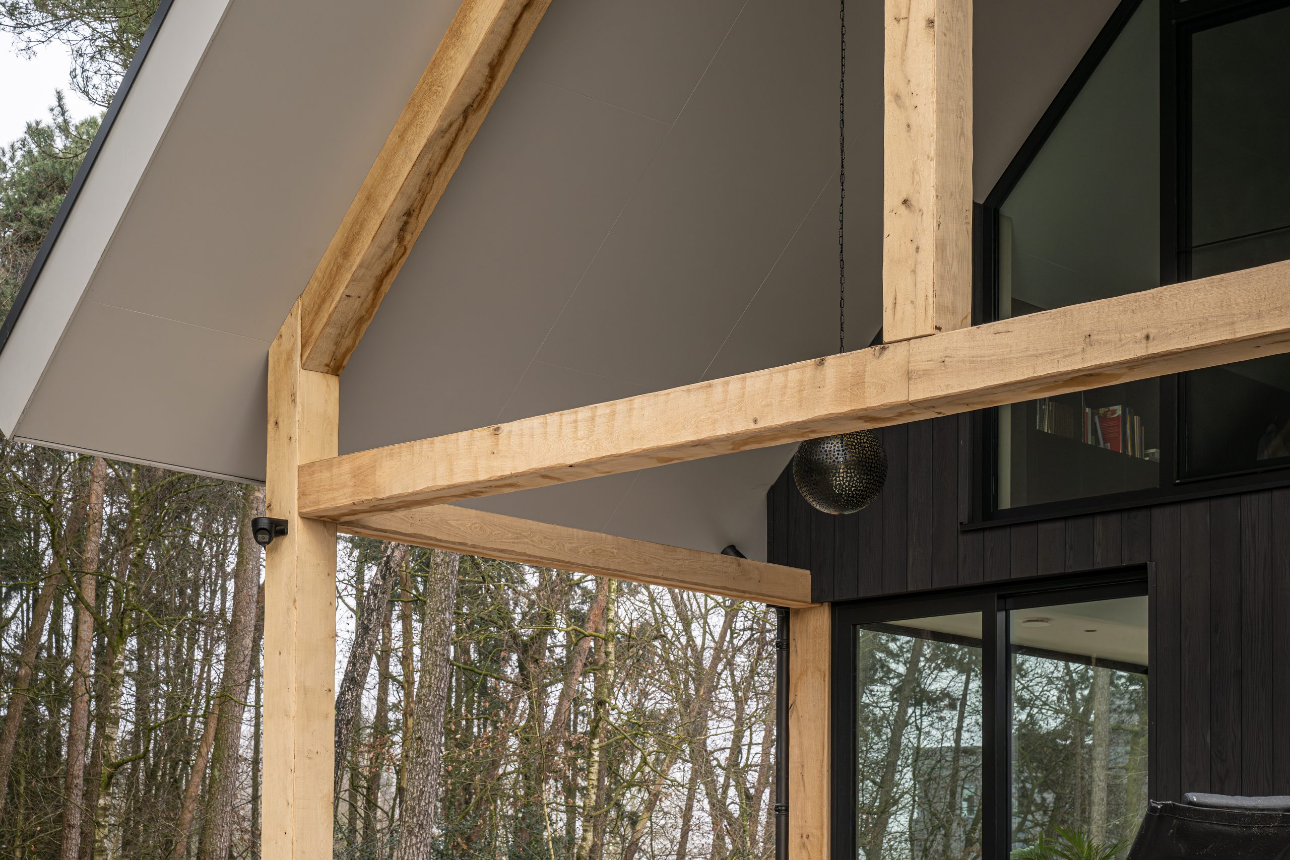 Sfeervol overdekt terras met eikenhouten balkomtimmeringen en twee decoratieve ronde hanglampen.