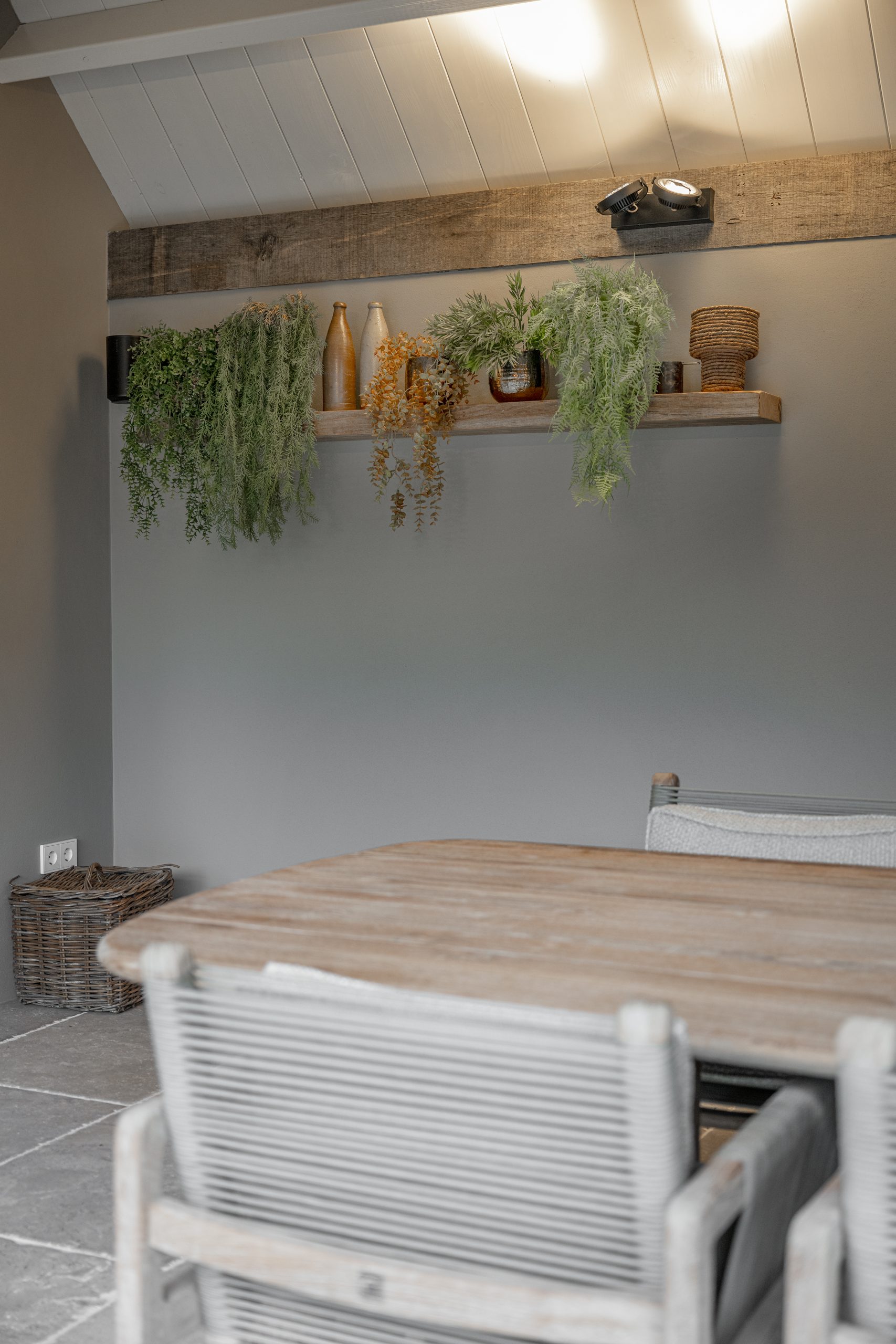 Sfeervolle wanddecoratie met diverse hangplanten en accessoires op een houten plank boven een eettafel.