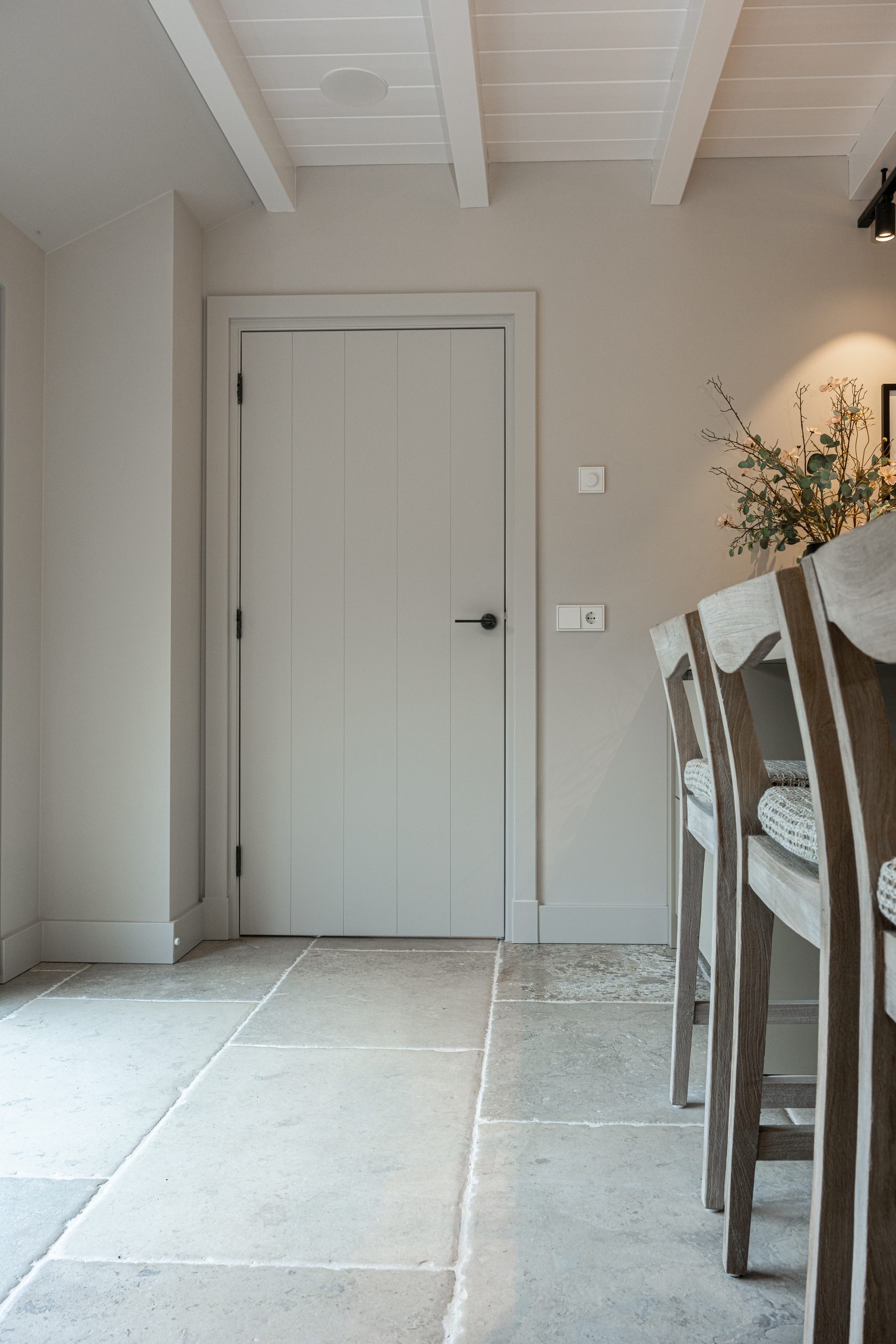 Gesloten witte binnendeur met verticale groeven en een moderne zwarte deurklink, staand op een lichte natuurstenen vloer.