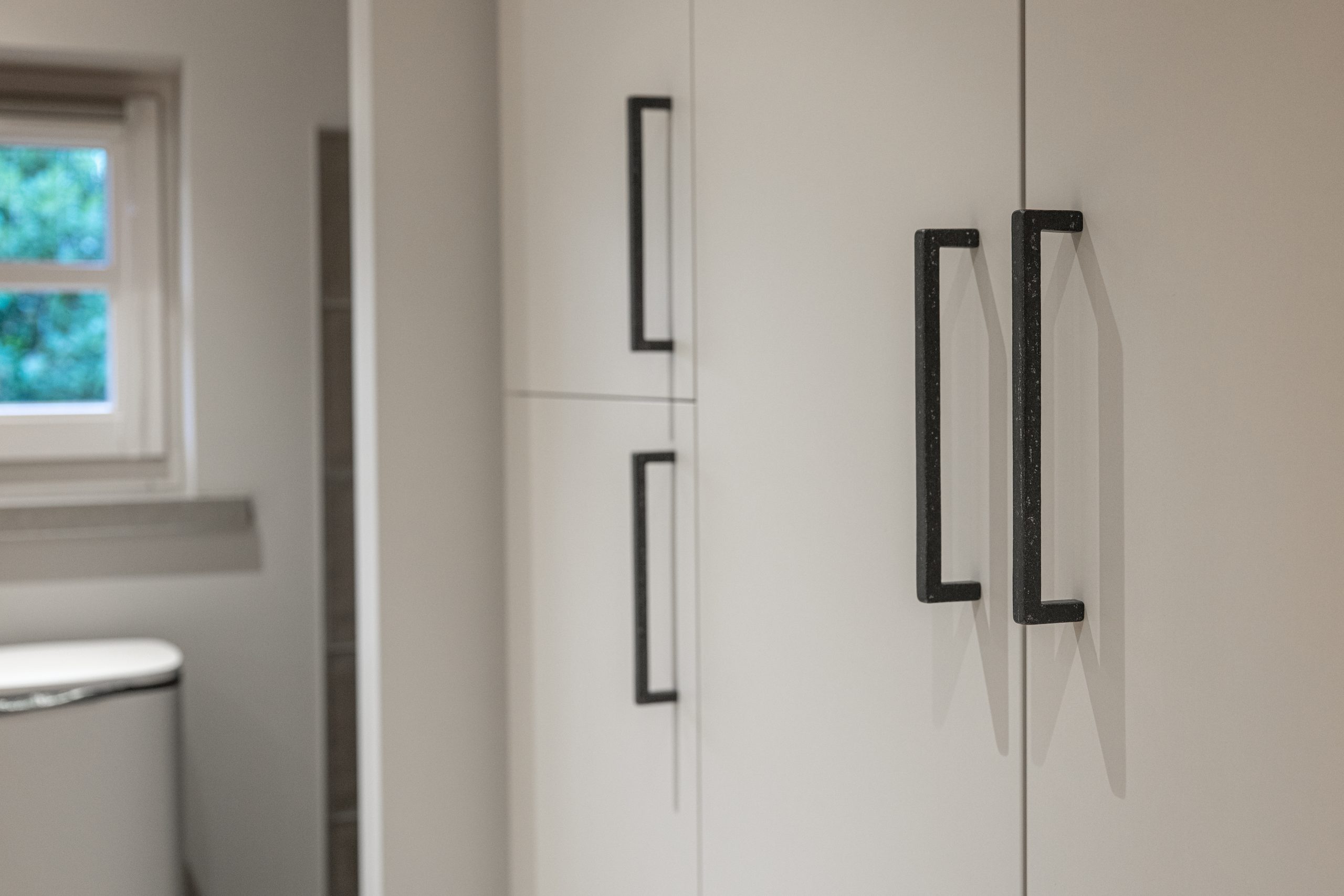 Close-up van lange, verticale zwarte grepen op de lichte deuren van een maatwerk kast.
