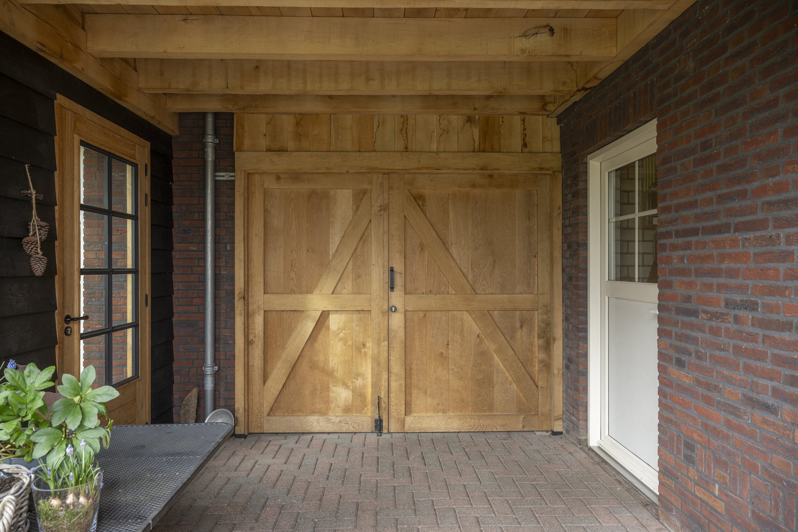 Een op maat gemaakte dubbele eikenhouten schuifpoort met een landelijke uitstraling, geplaatst onder een overkapping.