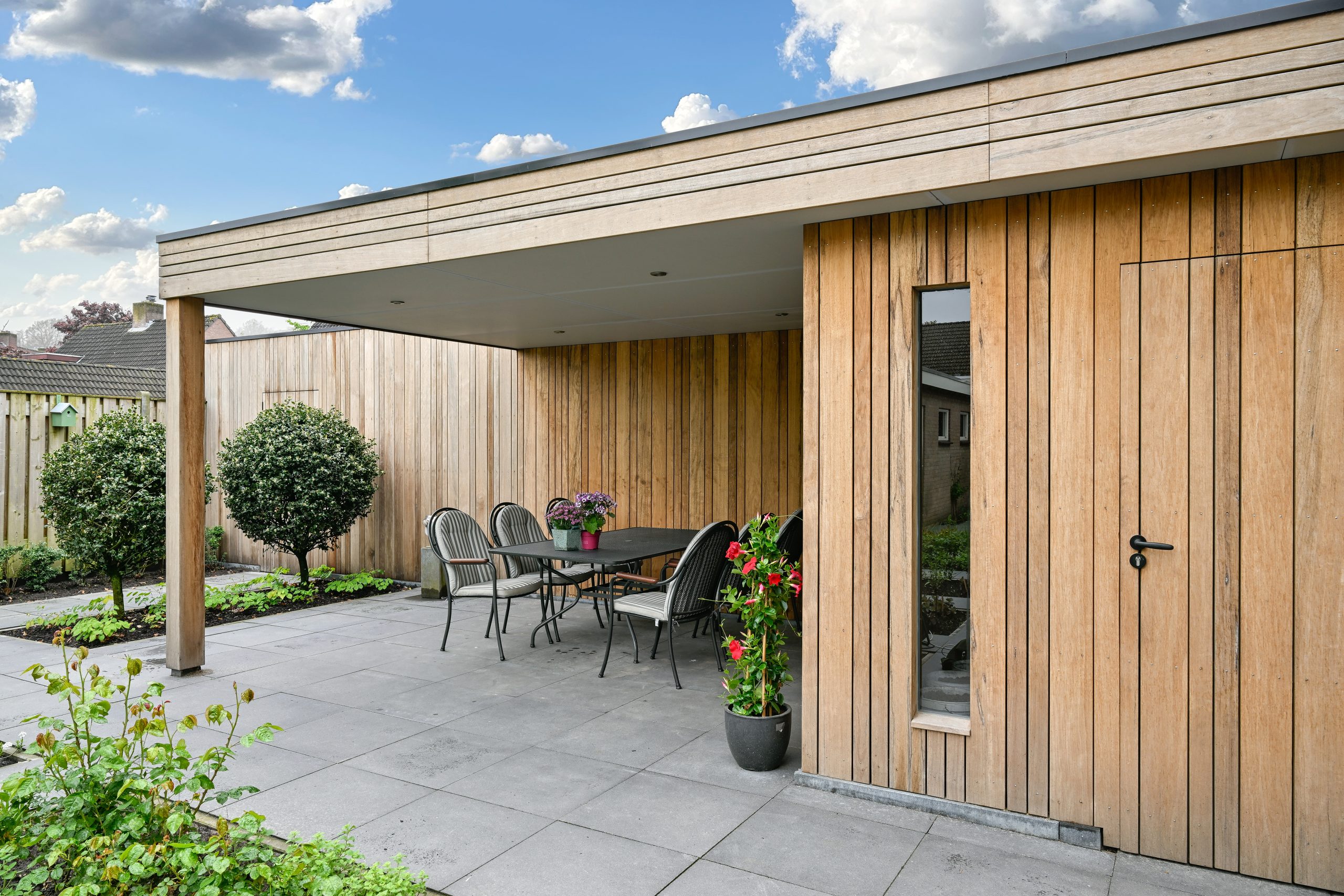 Close-up van de hoek van een houten overkapping met een smal verticaal raam en een zwarte deurklink.