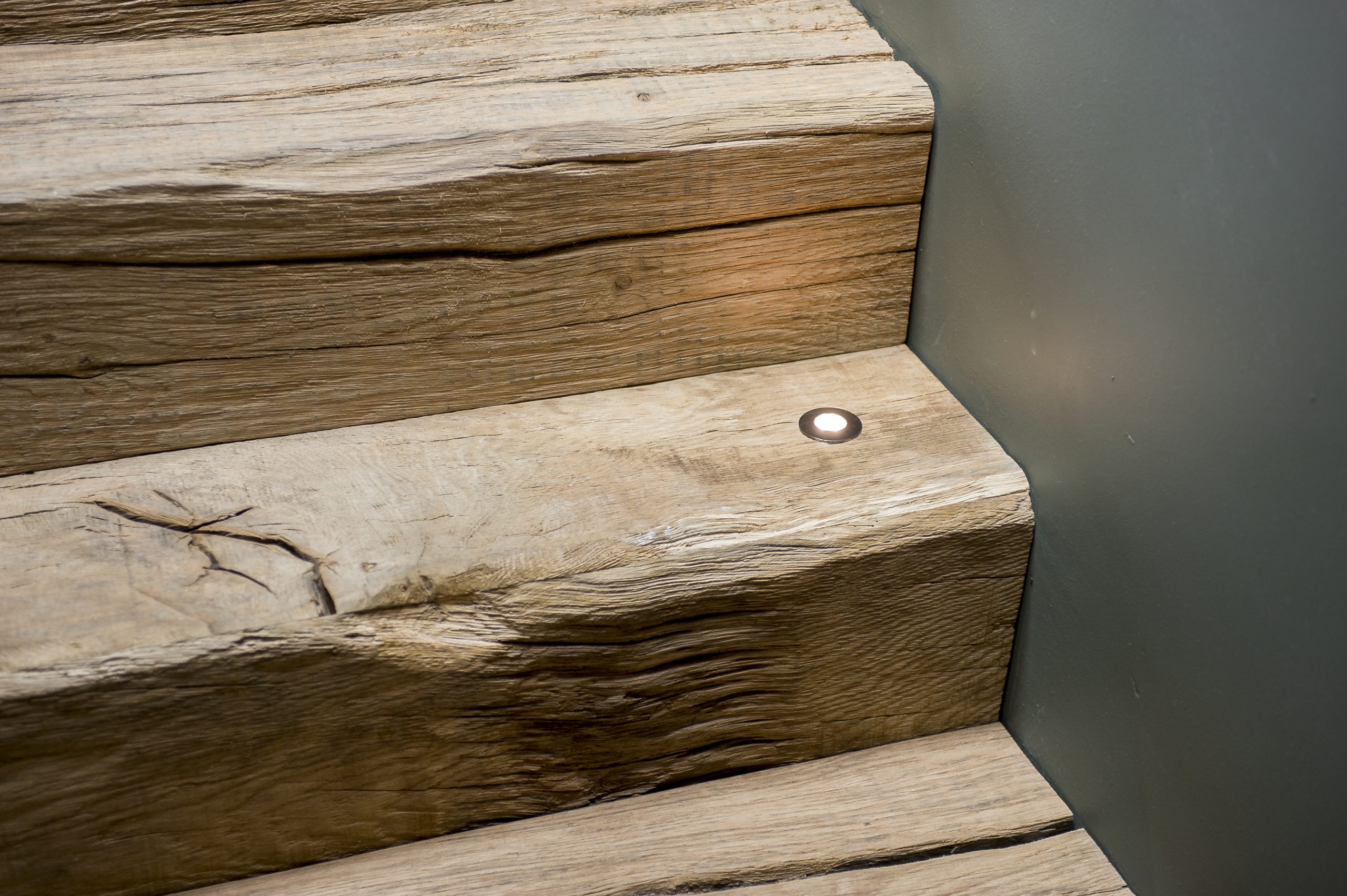 Close-up van de grove structuur en scheuren in de massieve eikenhouten traptreden met een ingebouwde spot.