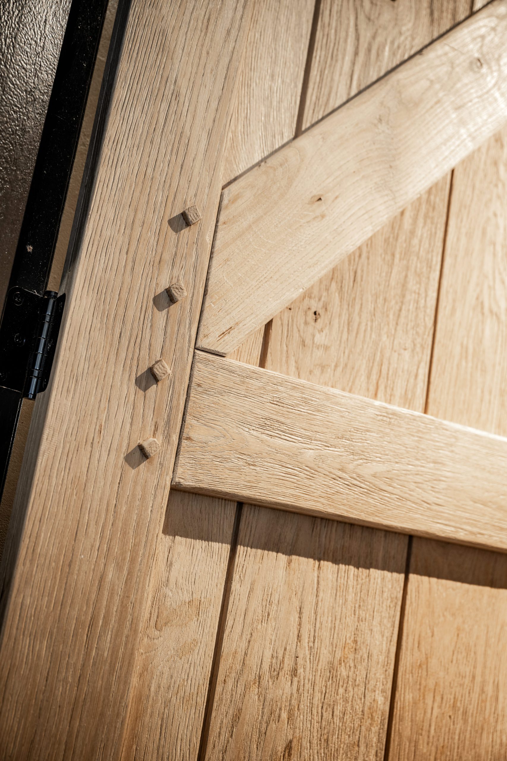 Close-up van een ambachtelijke eikenhouten deur met traditionele houten pennen (doken) en een zwart metalen scharnier.