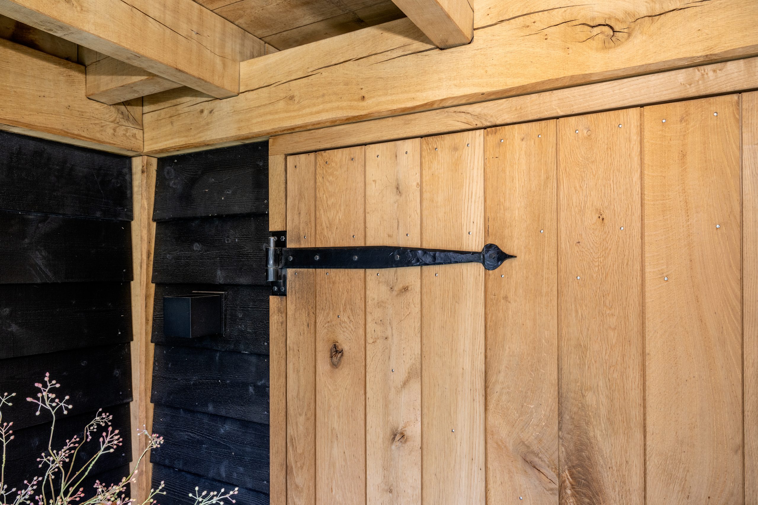 Detail van een klassiek zwart smeedijzeren scharnier op een robuuste eikenhouten deur.