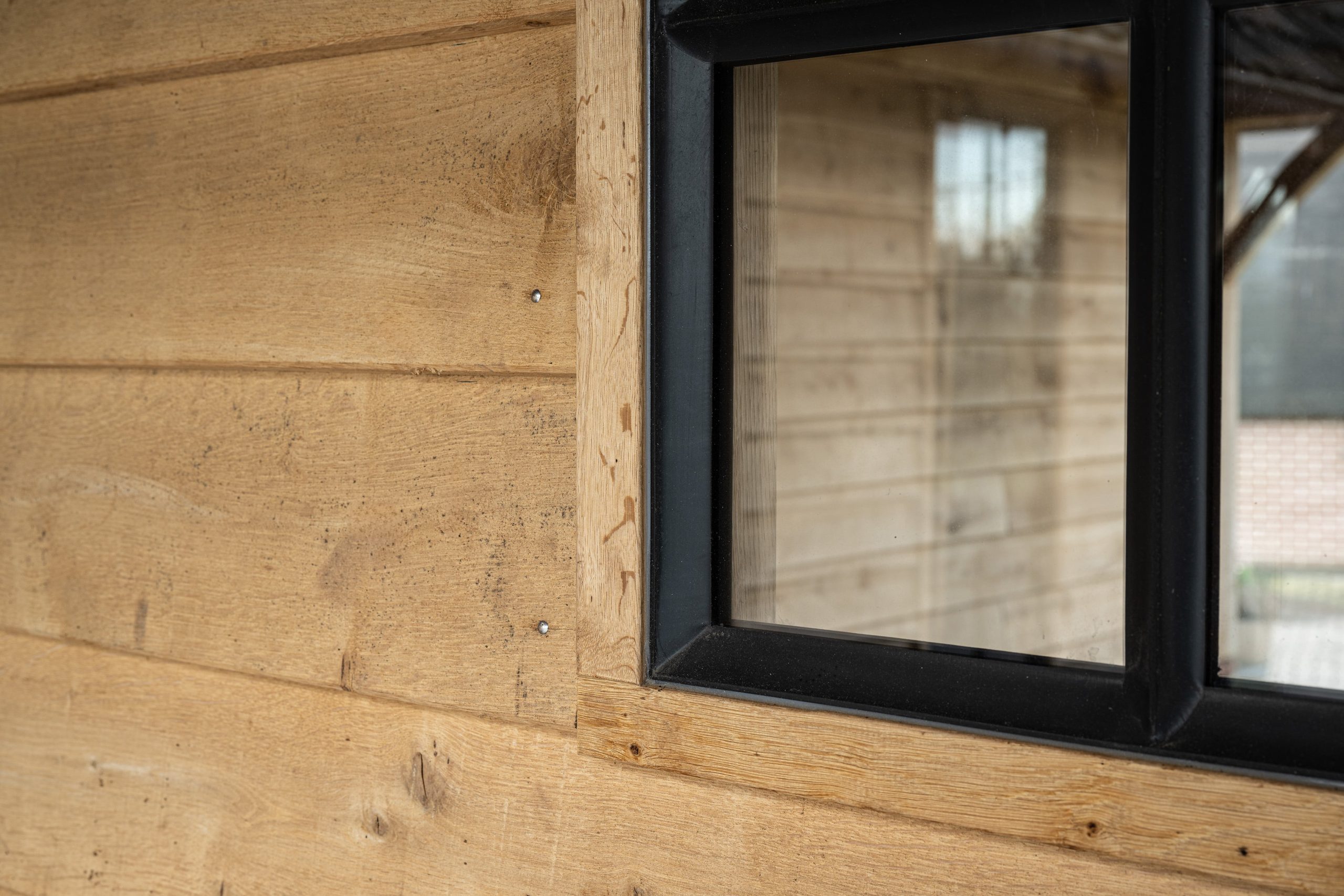 Close-up van een modern zwart stalen raamkozijn gemonteerd in een wand van robuuste eikenhouten planken