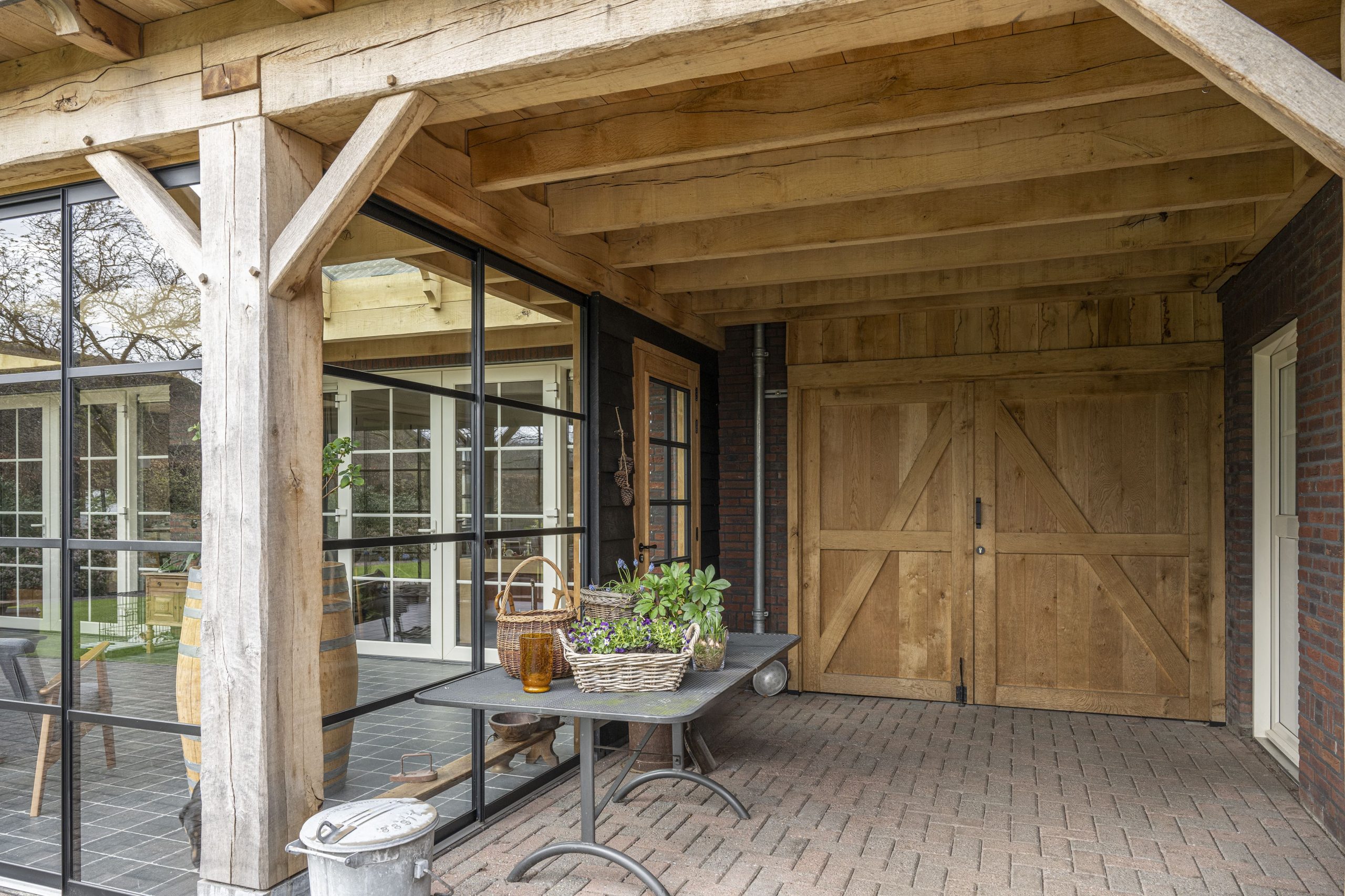 Grote, op maat gemaakte dubbele schuifpoort van eikenhout met zwart beslag, passend in een landelijke stijl.