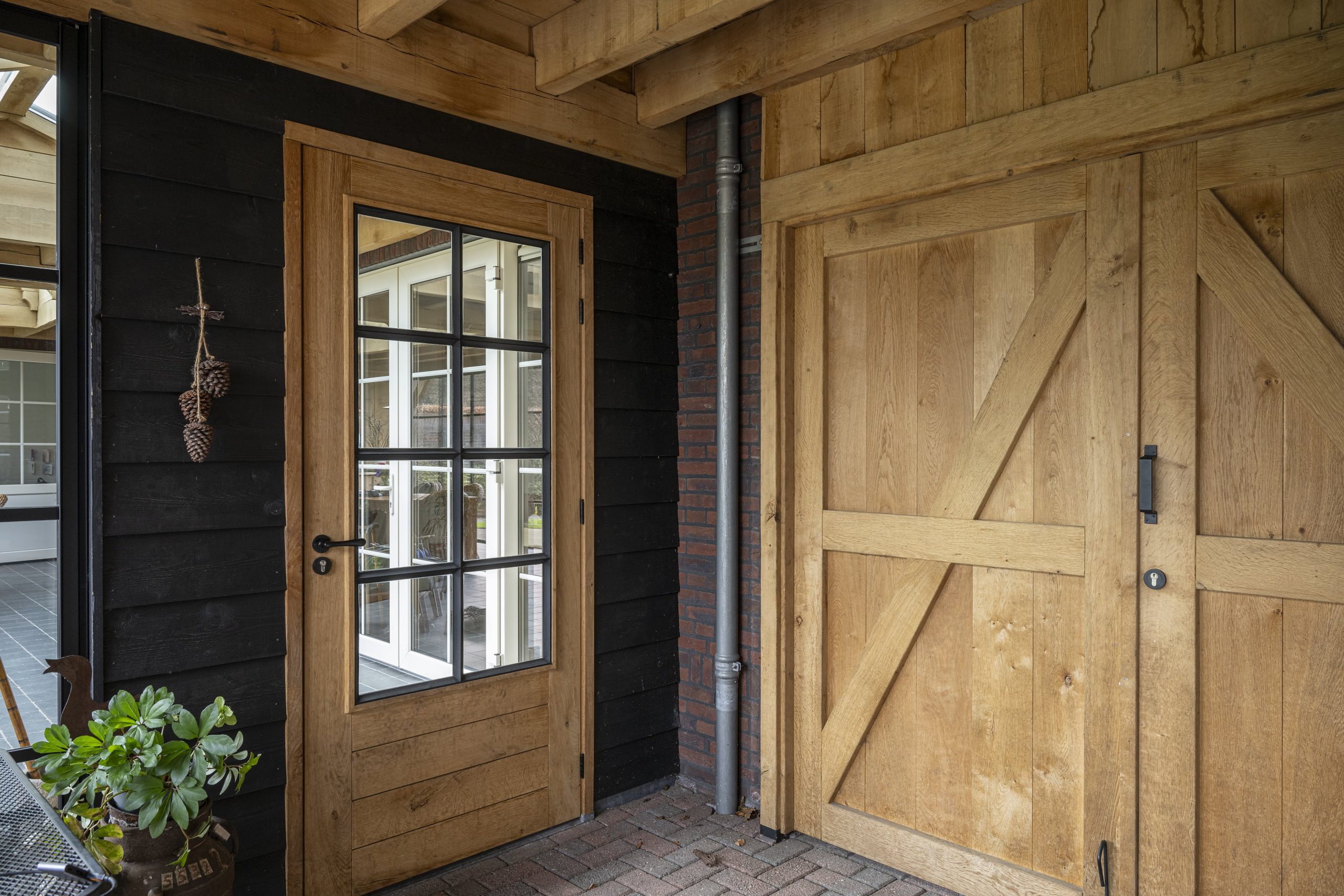 Een eikenhouten deur met glas geplaatst in een moderne zwarte houten wand onder een overkapping.