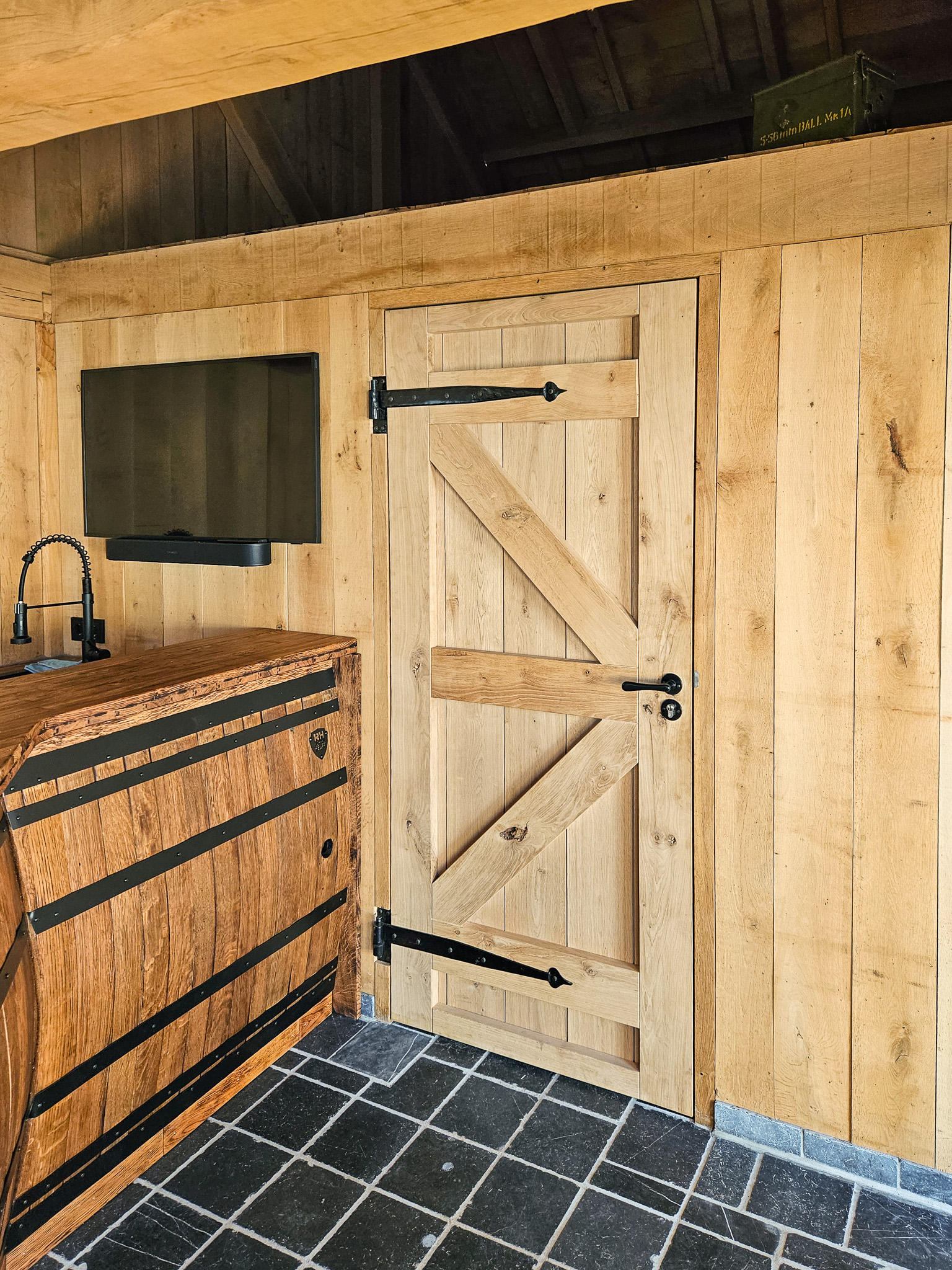 Binnenzicht van een massief eikenhouten deur met zwart landelijk beslag in een houten bijgebouw.