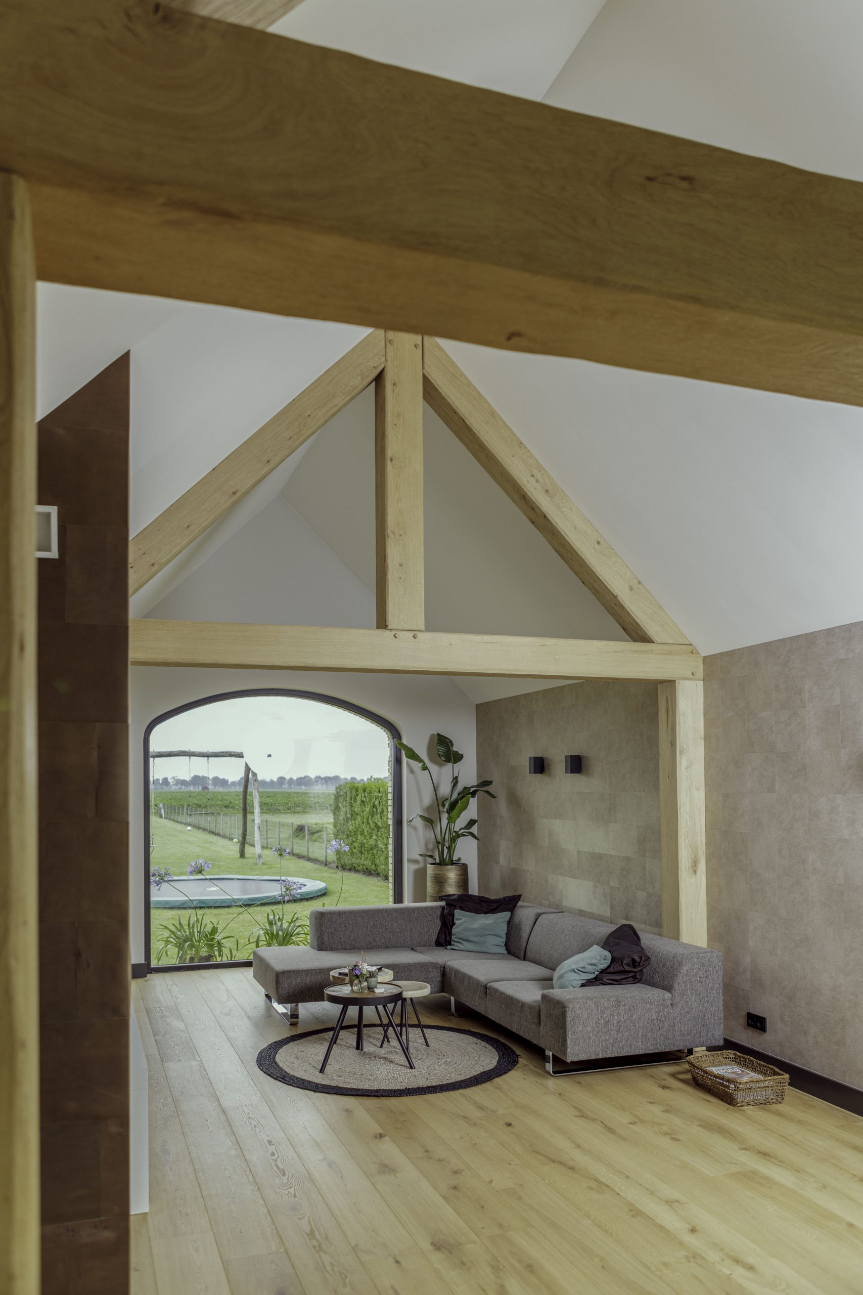 Zijaanzicht van een robuuste eikenhouten dakconstructie boven een zithoek met een modern grijs interieur.