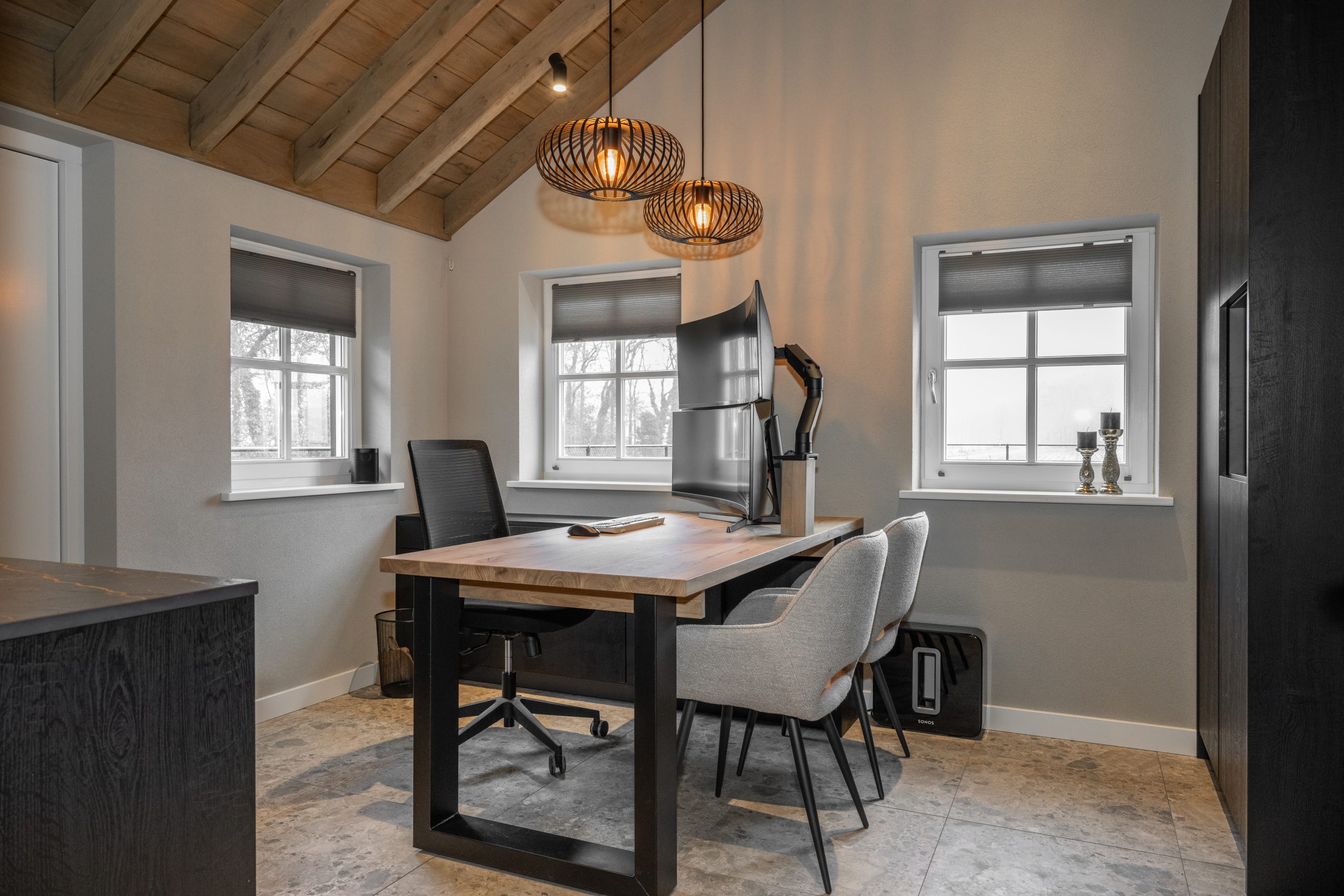 Maatwerk eikenhouten bureau in een modern kantoor met een hoog balkenplafond, zwarte kasten en grijze designstoelen.
