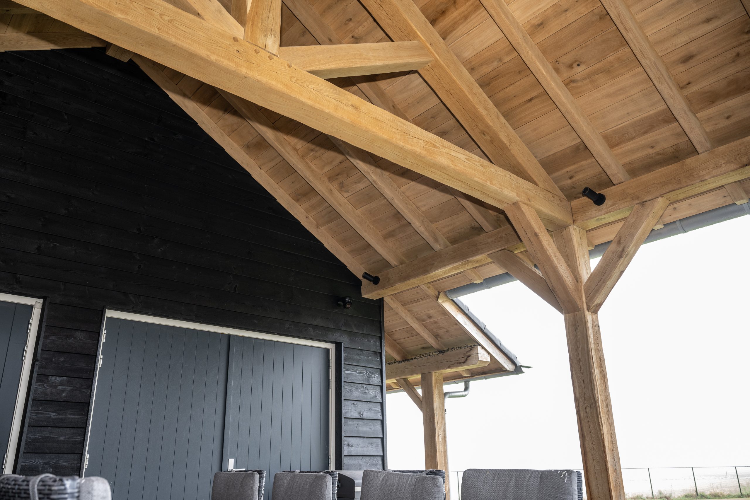Zicht op het indrukwekkende eikenhouten dakbeschot en de dragende balkenstructuur van een luxe veranda of tuinhuis.