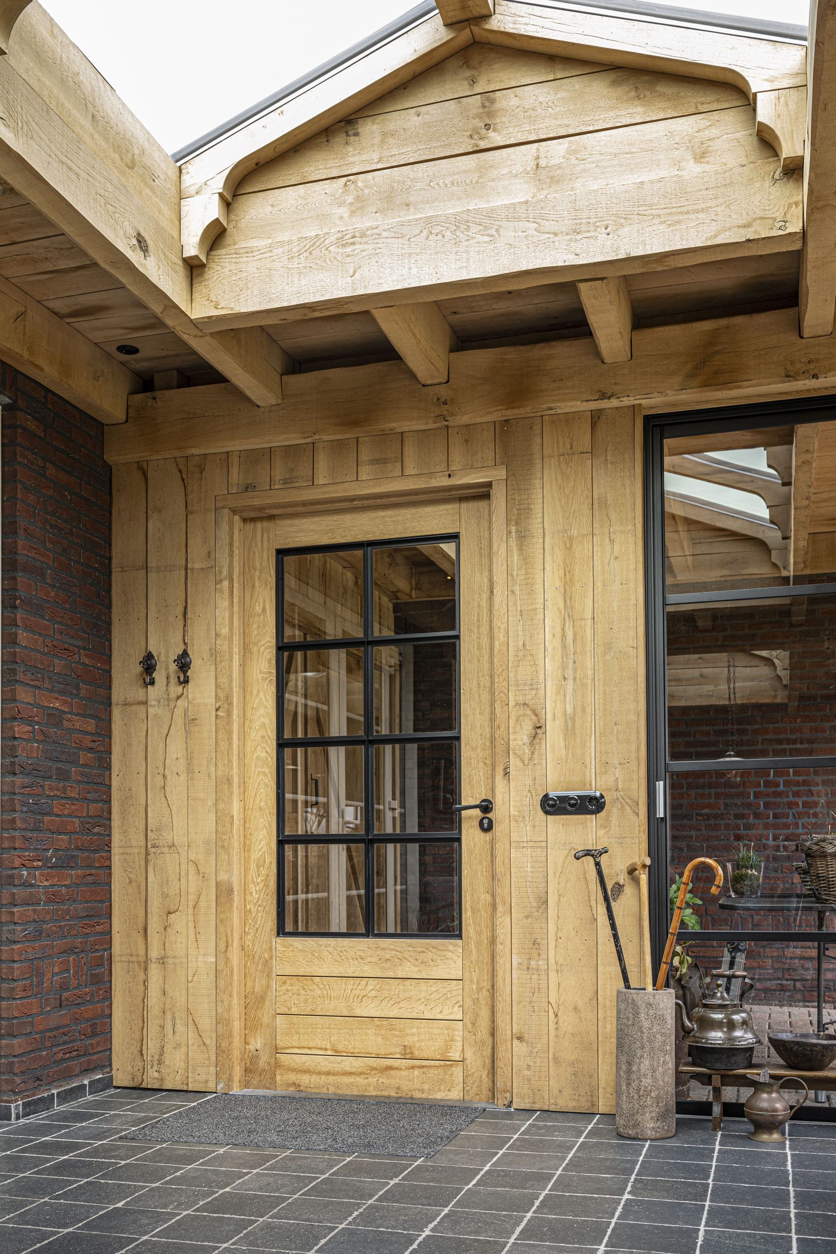Close-up van een ambachtelijke eikenhouten loopdeur met glazen ruiten en zwart beslag, verwerkt in een houten wand.