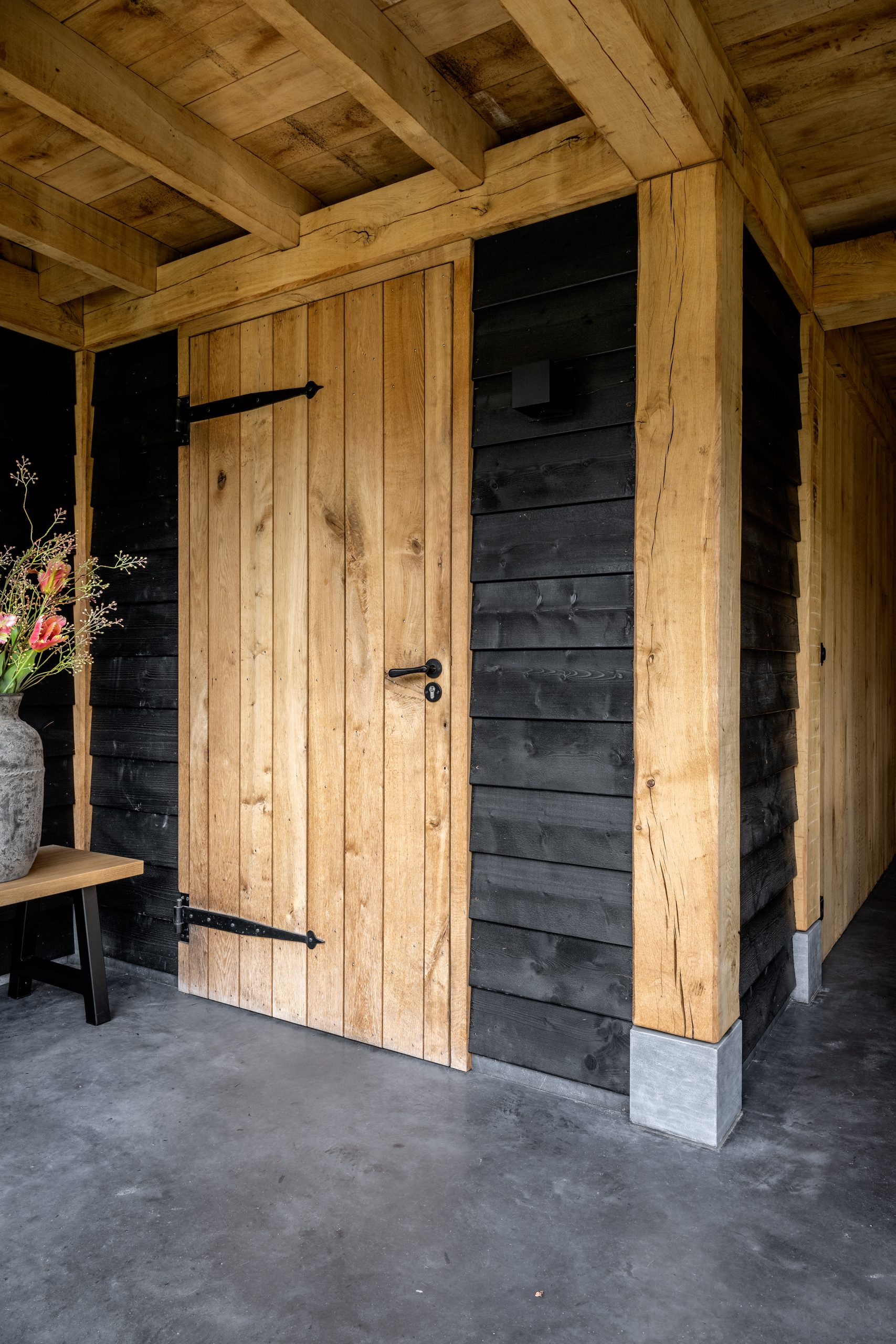 Close-up van een eikenhouten deur met zwart beslag in een tuinhuis met zwarte potdekselplanken.