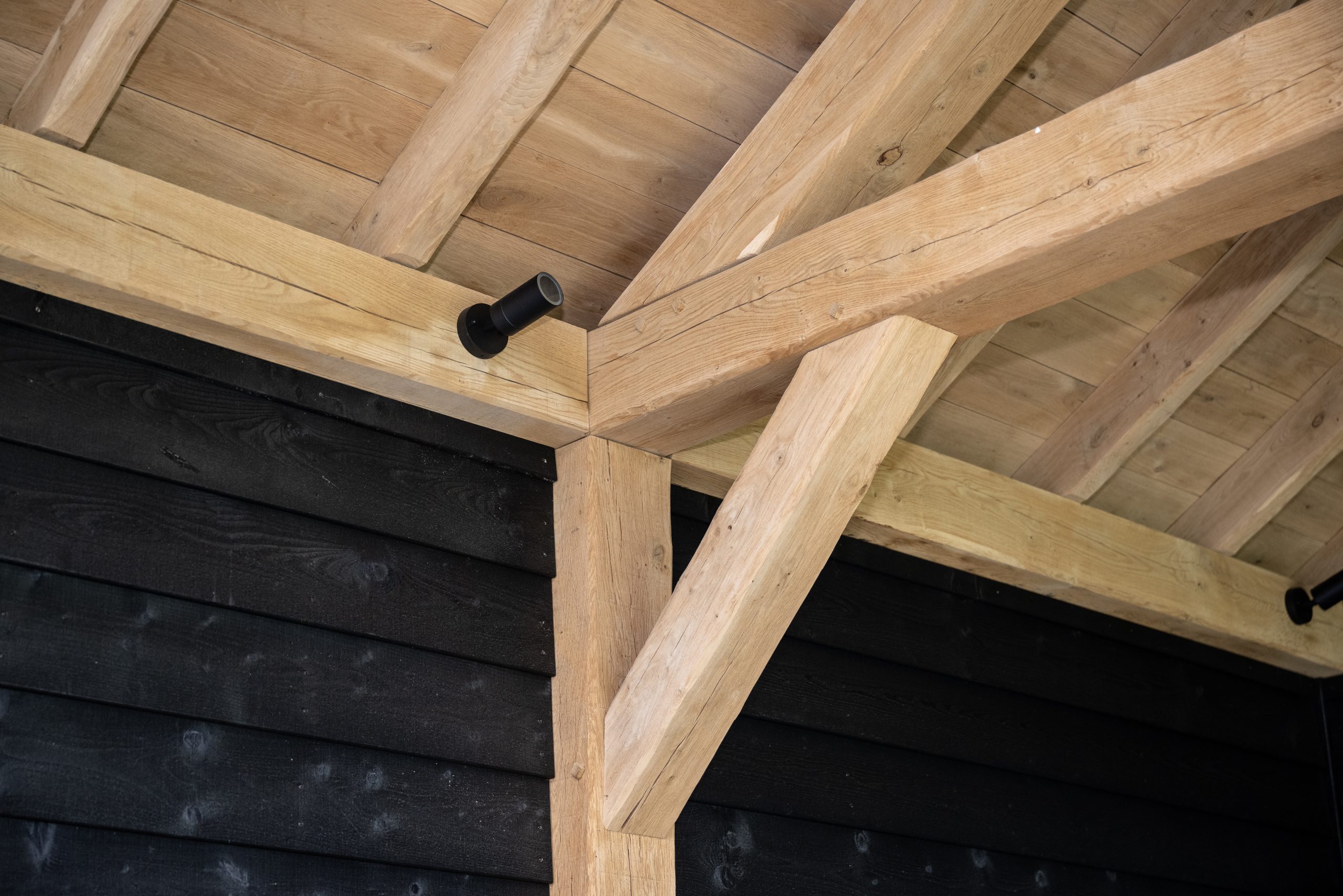 Detailopname van een robuuste eikenhouten paal met traditionele pen-en-gatverbinding onder een luxe overkapping.