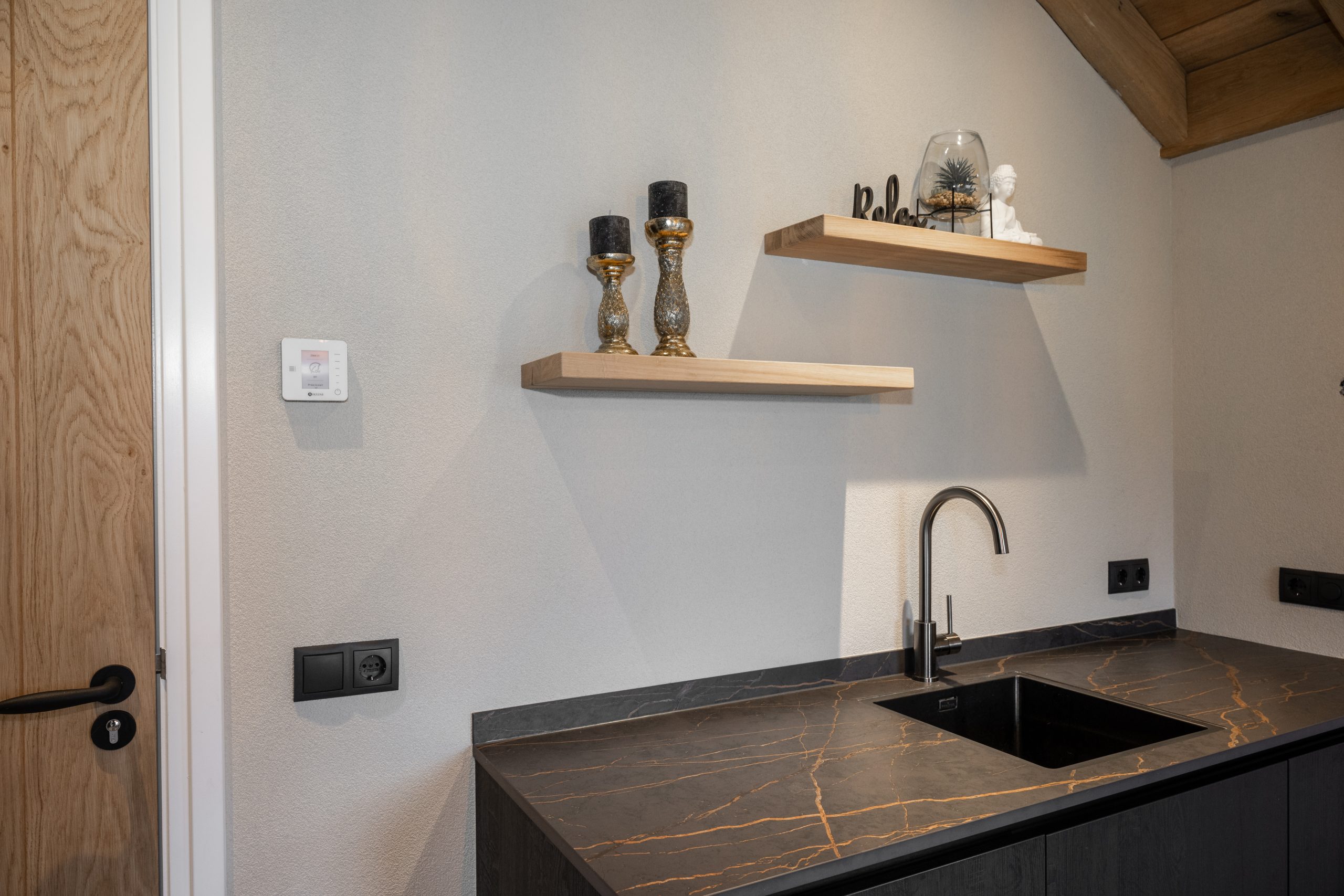 Detail van zwarte keuken met marmerlook blad en zwevende eikenhouten wandplanken tegen een lichtgrijze wand.