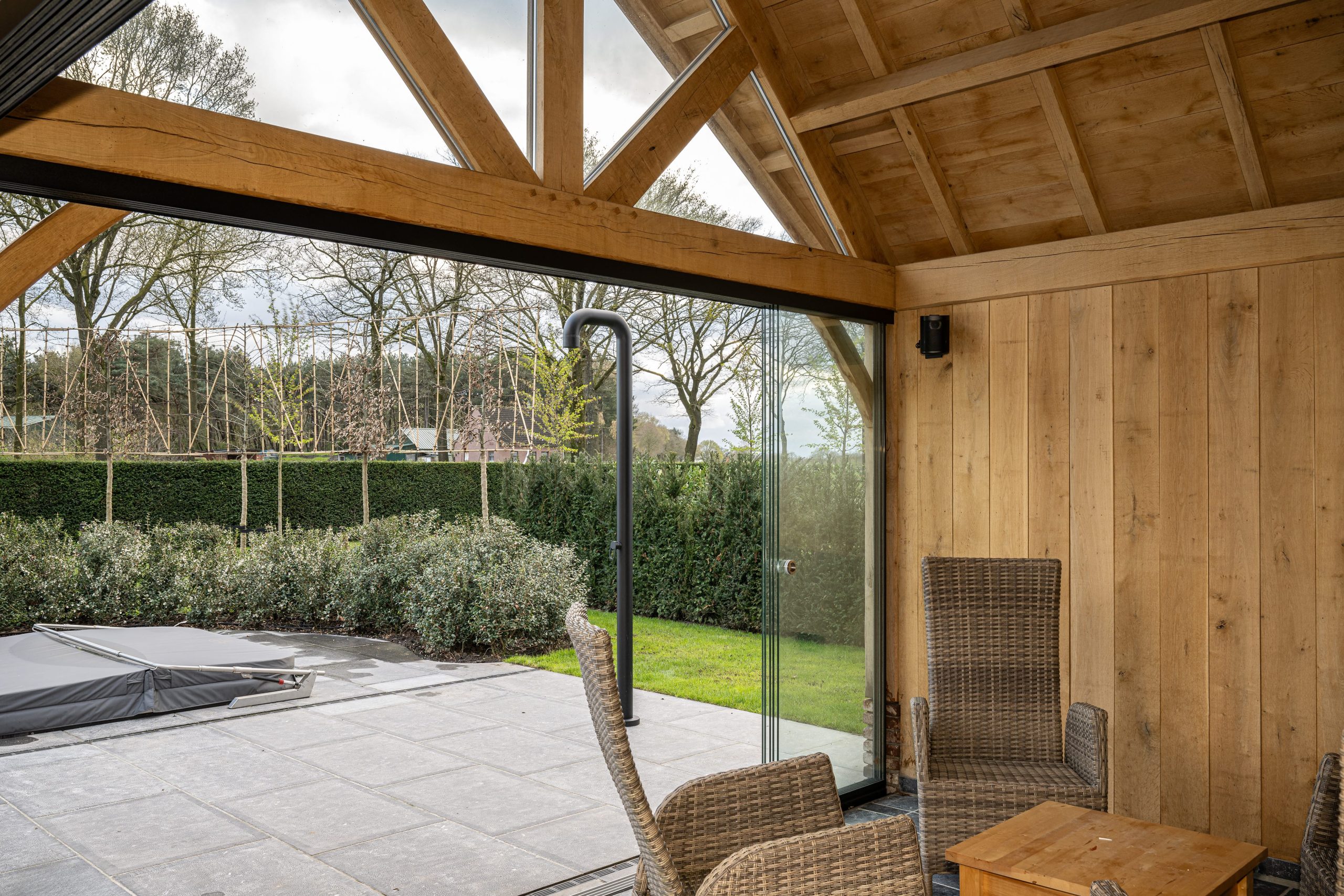 Interieur van een houten overkapping met uitzicht op de tuin door glazen schuifwanden.