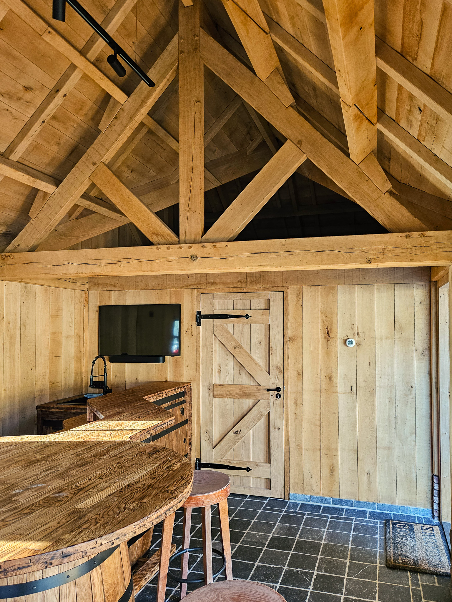 Overzicht van het interieur van een tuinhuis met een bar, tv-scherm aan de wand en sfeervolle verlichting.