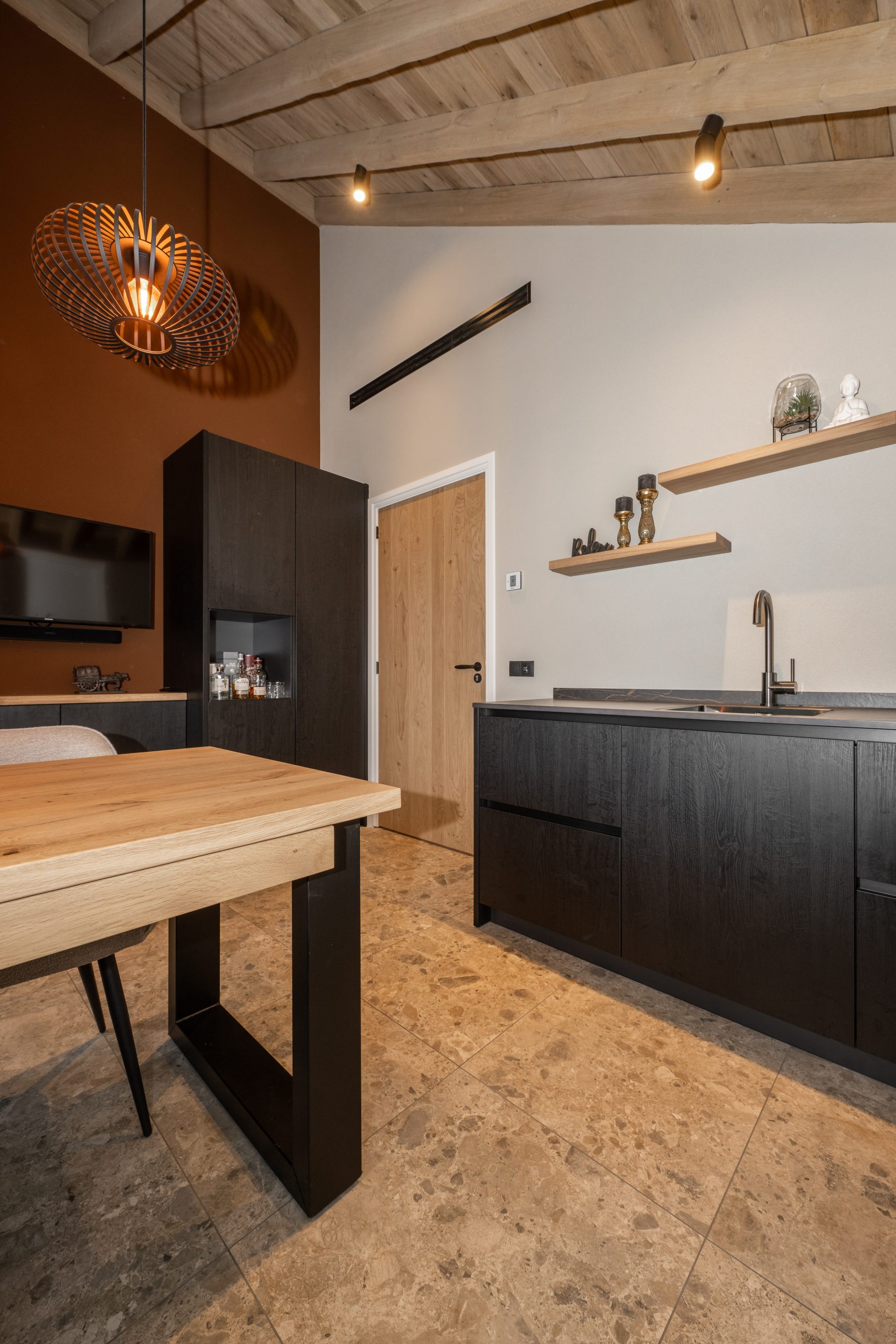 Werkkamer met een luxe zwarte pantry, eikenhouten plafondbalken, een houten binnendeur en een warme terra-kleurige accentmuur.