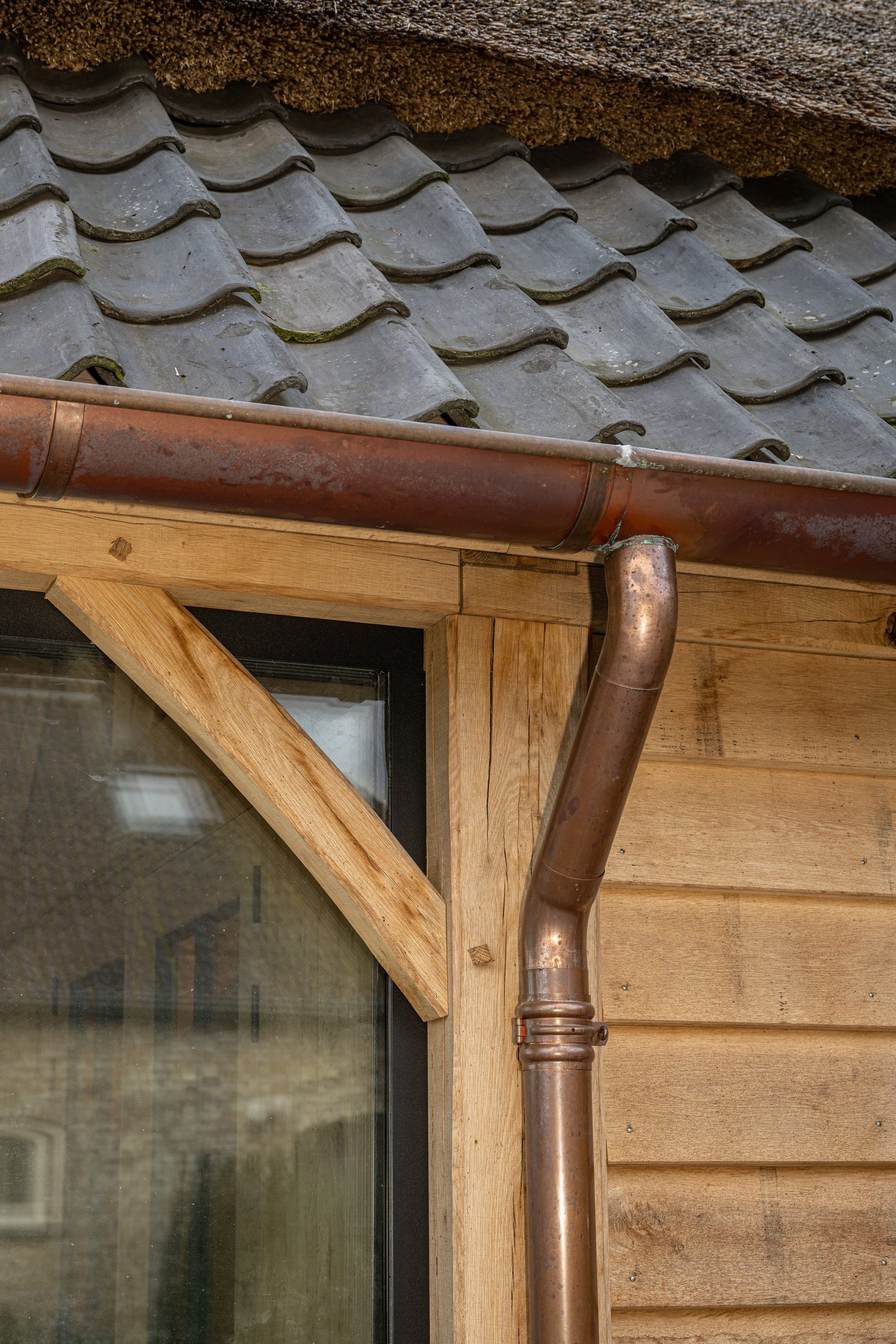 Detail van een koperen dakgoot en regenpijp op een eikenhouten overkapping.