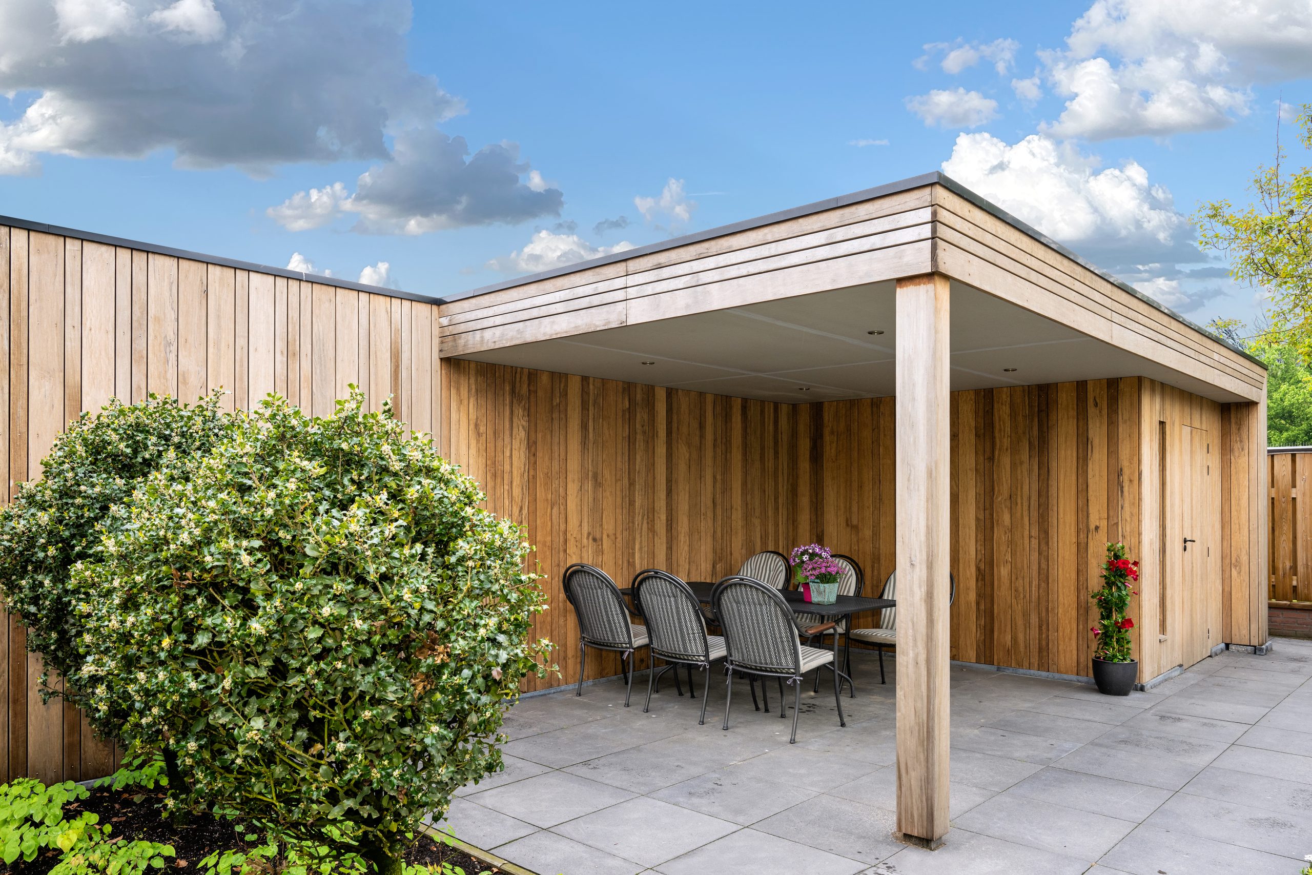 Zijaanzicht van een houten overkapping met een eethoek en een strakke afwerking van verticale houten latten.