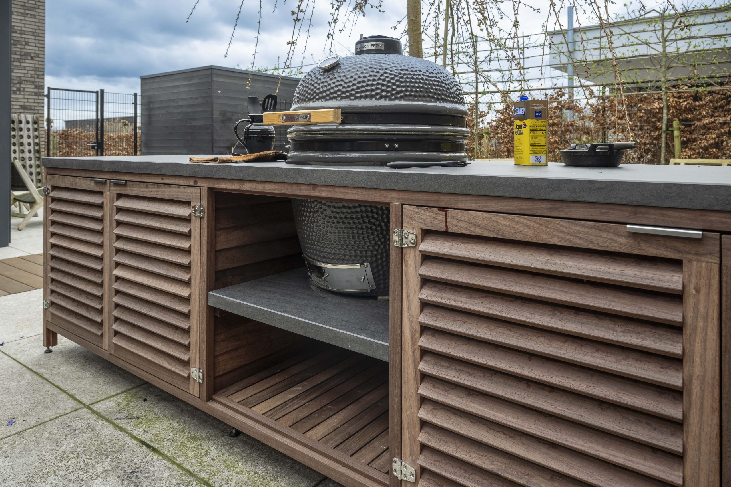 Luxe padoek houten buitenkeuken met een ingebouwde zwarte kamado barbecue en een stenen werkblad.
