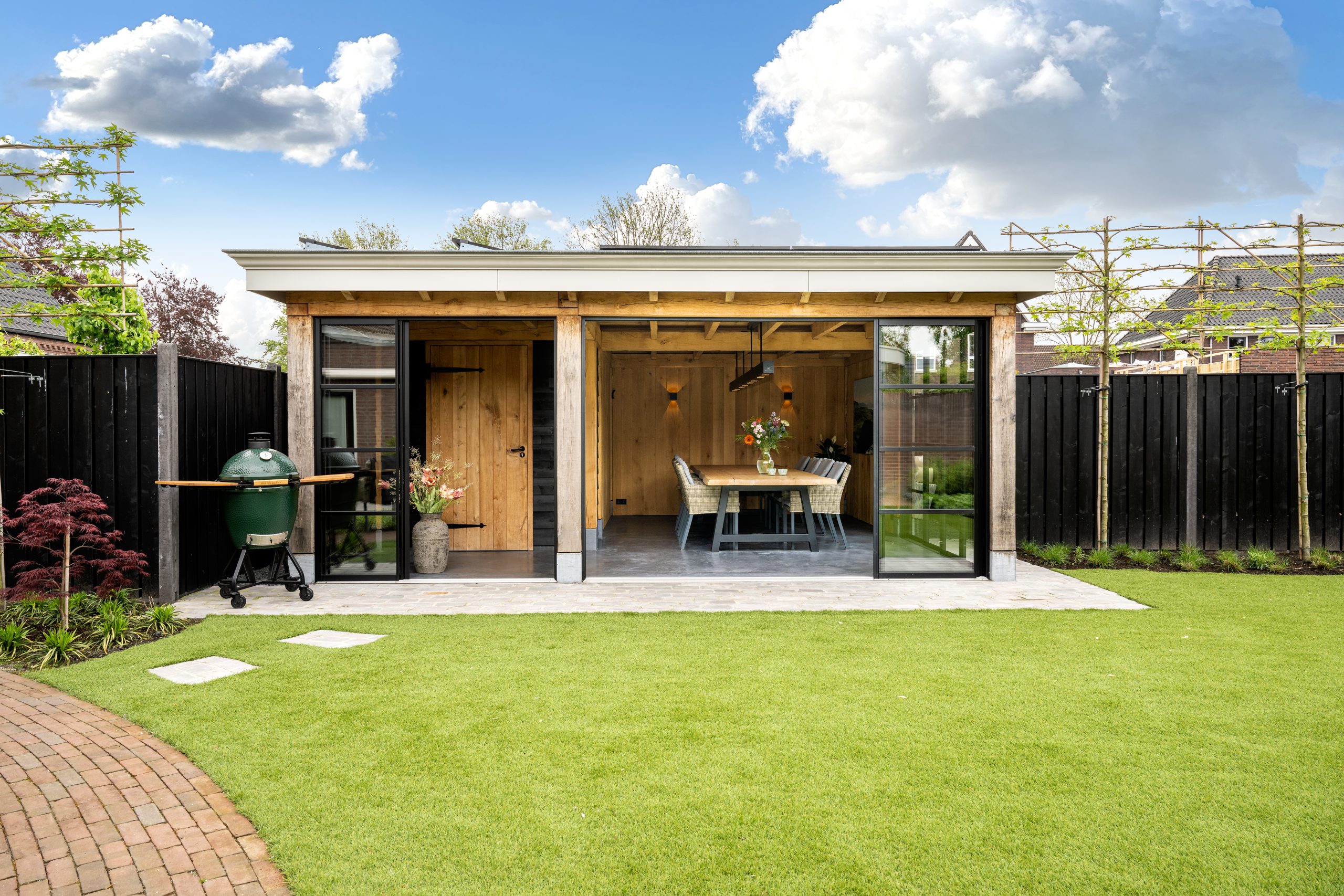 Luxe eikenhouten buitenverblijf met plat dak en glazen puien in een zonnige achtertuin.