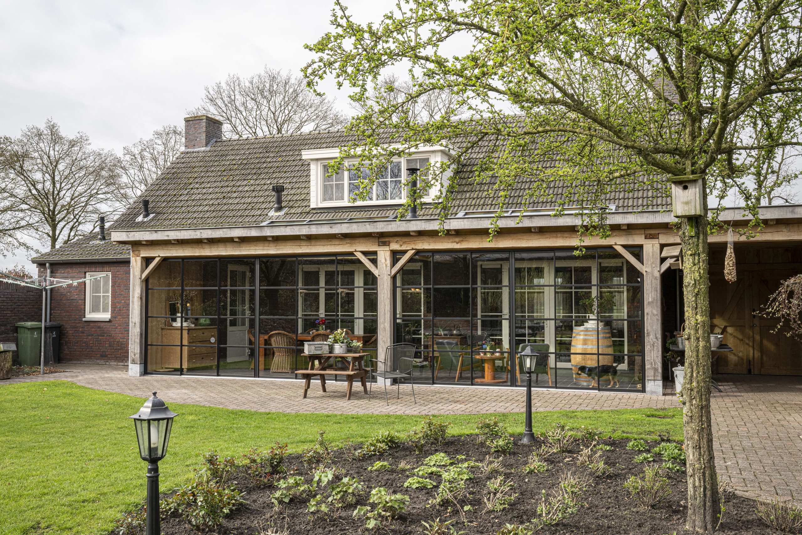 Vooraanzicht van een luxe eikenhouten overkapping met glazen schuifwanden, aangebouwd aan een landelijke woning.