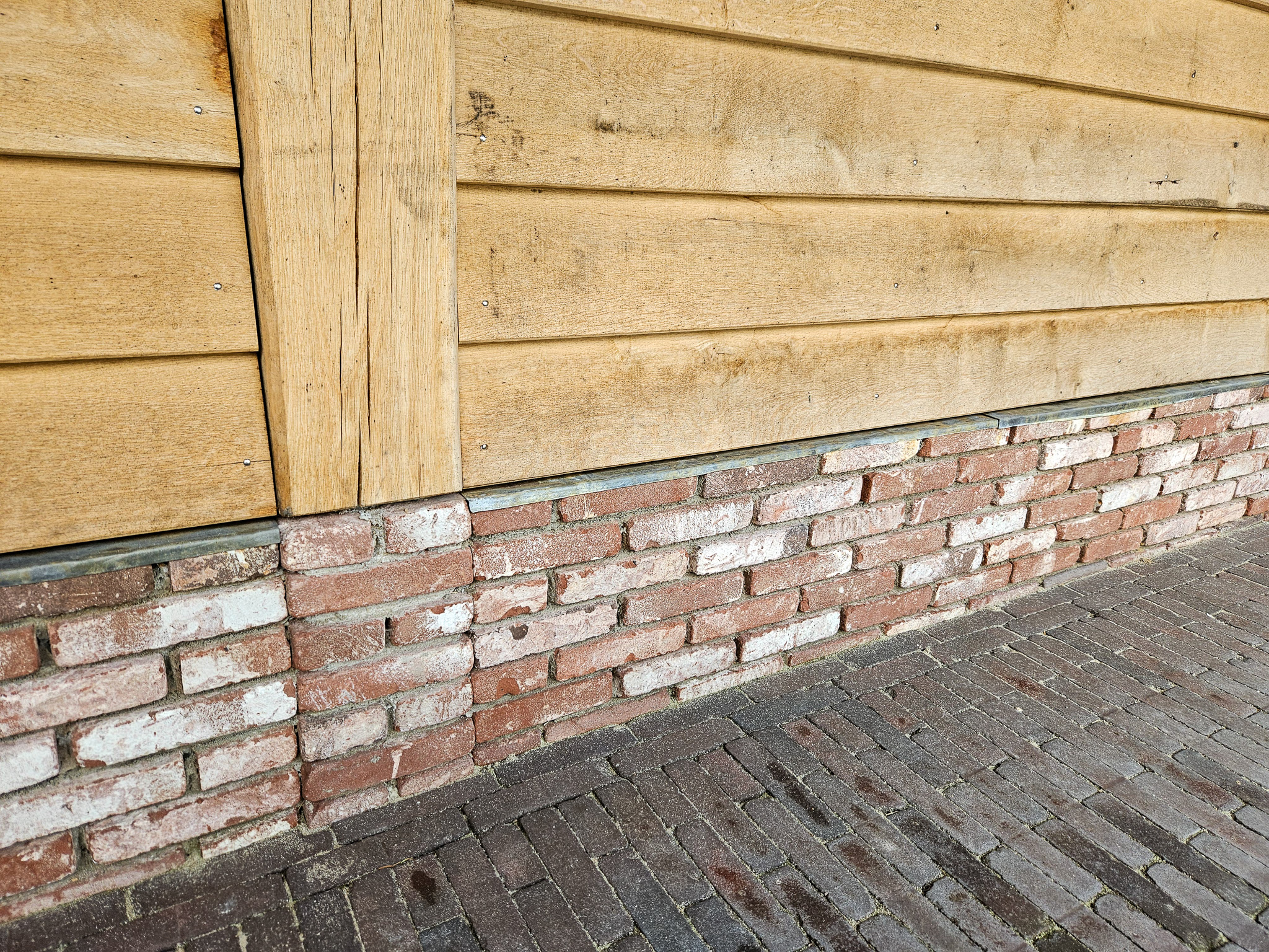 Detail van de gemetselde plint onder een eikenhouten gevelwand van een bijgebouw.