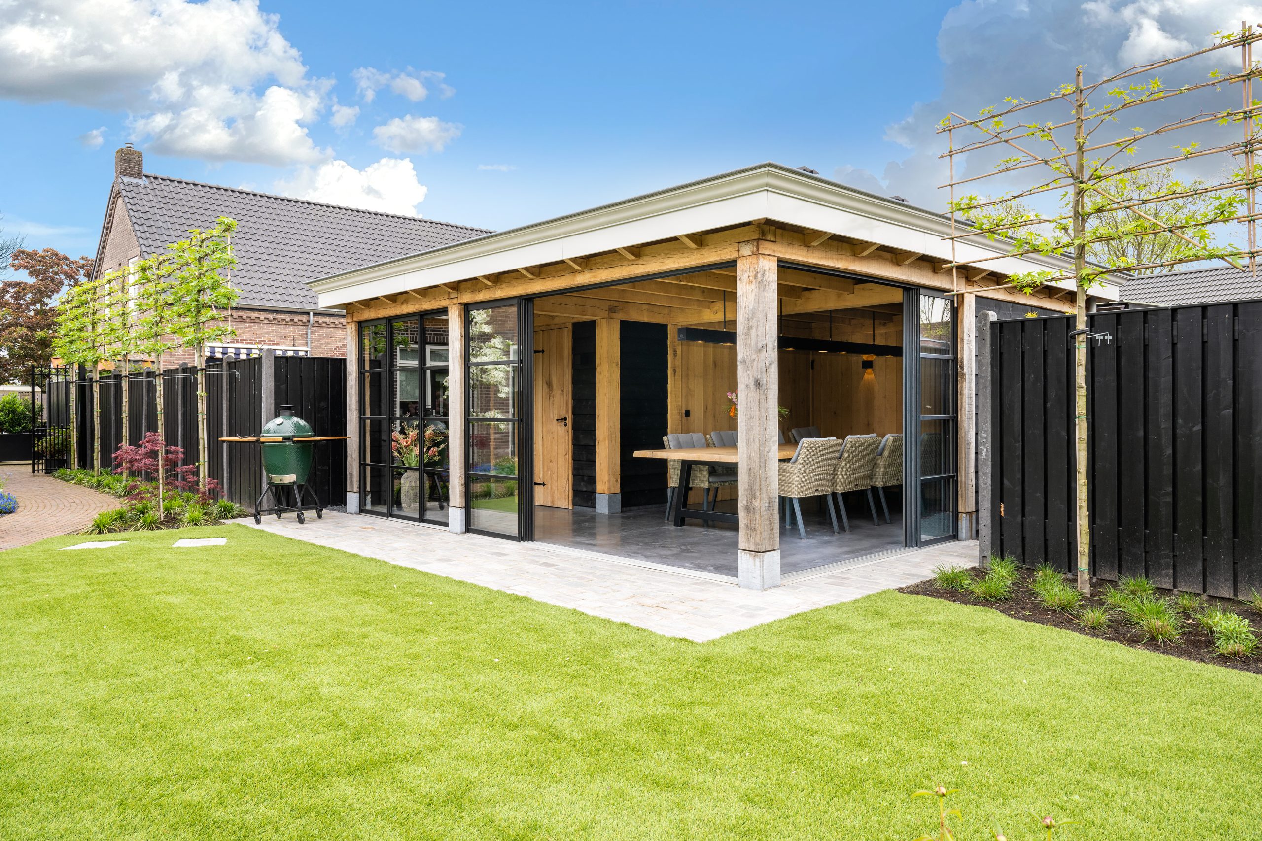 Modern eikenhouten buitenverblijf met glazen schuifwand in een strak aangelegde tuin met gazon.