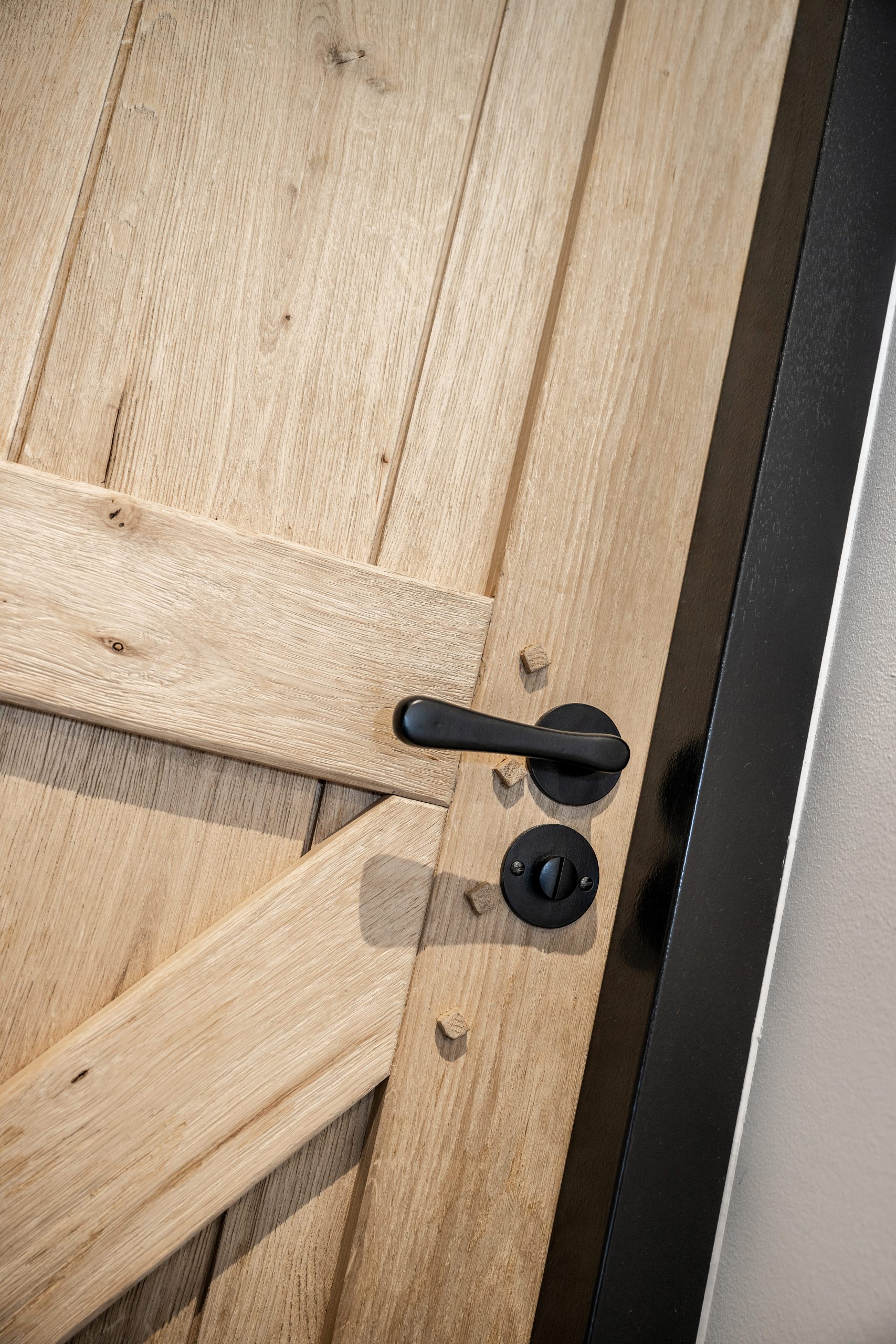 Detail van een modern zwart deurklink en slot op een landelijke eikenhouten deur met een zwart geverfd kozijn.