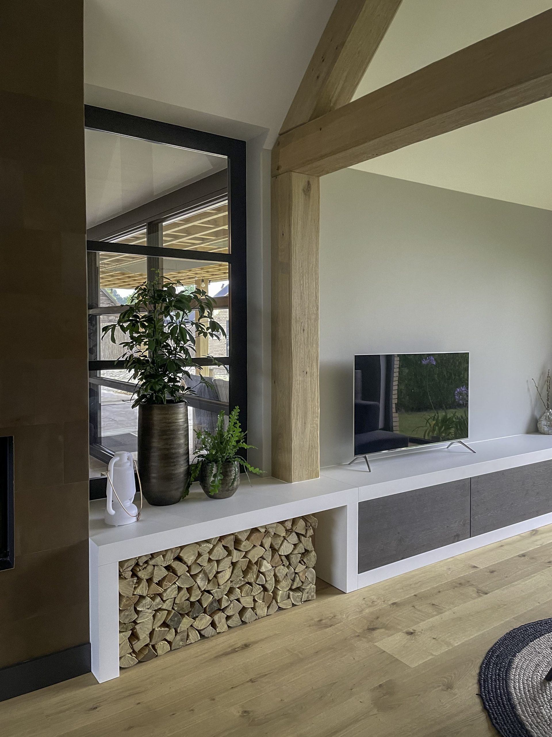 Detail van een wit op maat gemaakt tv-meubel met nis voor haardhout onder een massieve eikenhouten staander.