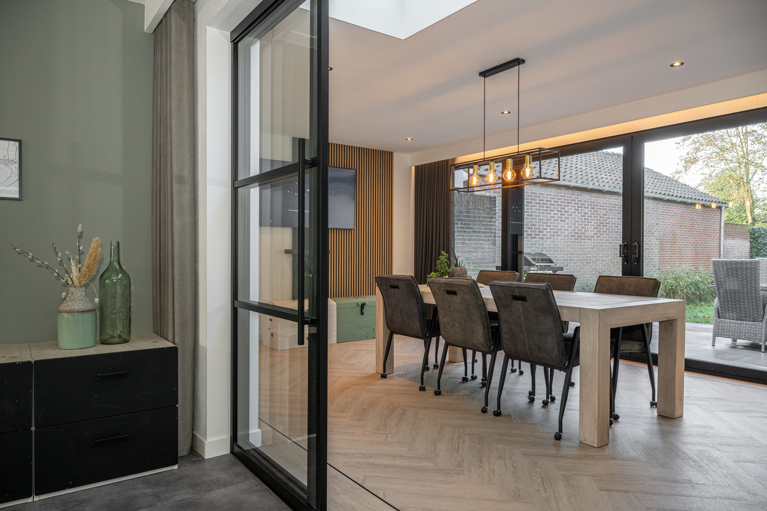 Gedeeltelijk geopende zwarte stalen schuifdeuren die zorgen voor een open verbinding tussen twee ruimtes.
