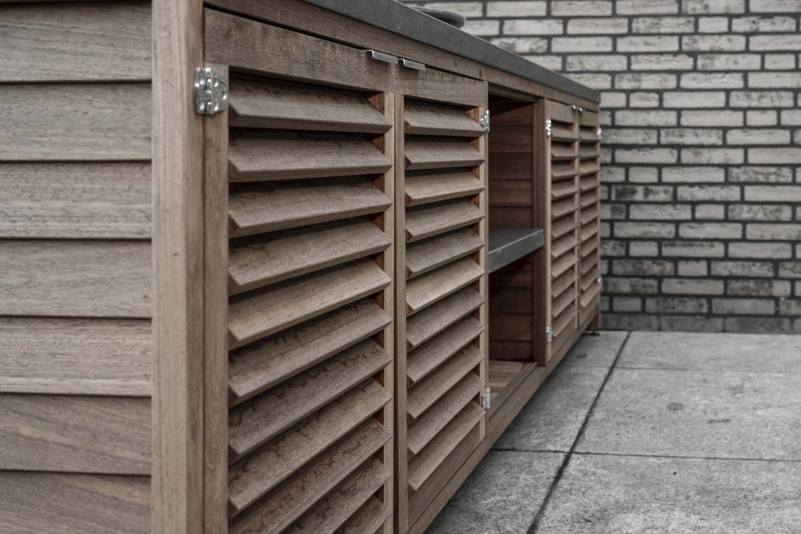 Close-up van een houten buitenkeuken met louvre-deurtjes van padoek hout en zilveren scharnieren.