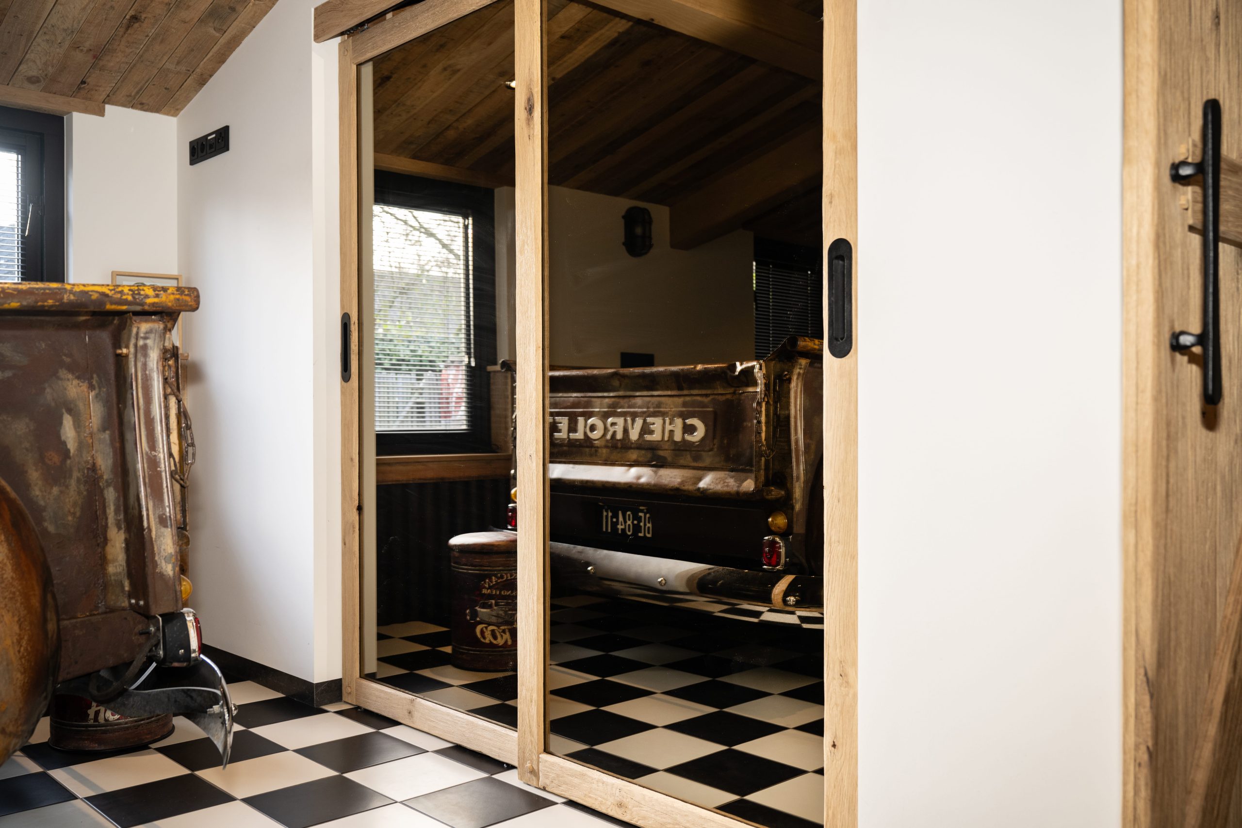 Achteraanzicht van een vintage Chevrolet pick-up truck, weerspiegeld in een kamerhoge spiegelwand met houten frame.