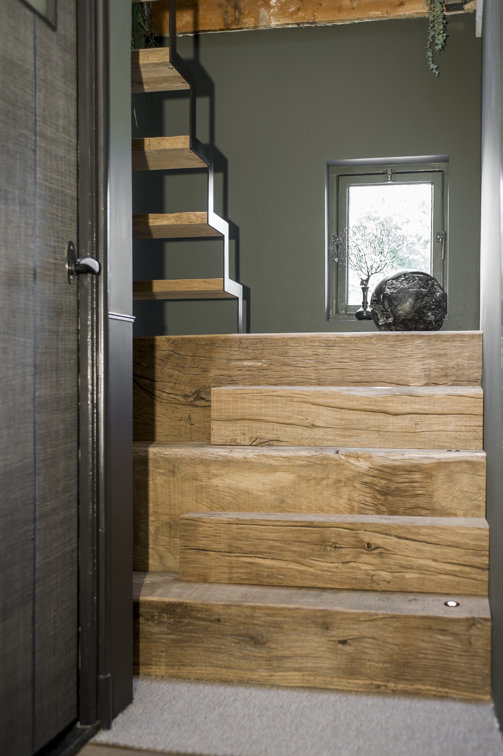 Vooraanzicht van een op maat gemaakte trap van gestapelde robuuste eikenhouten balken met ingebouwde spotjes.