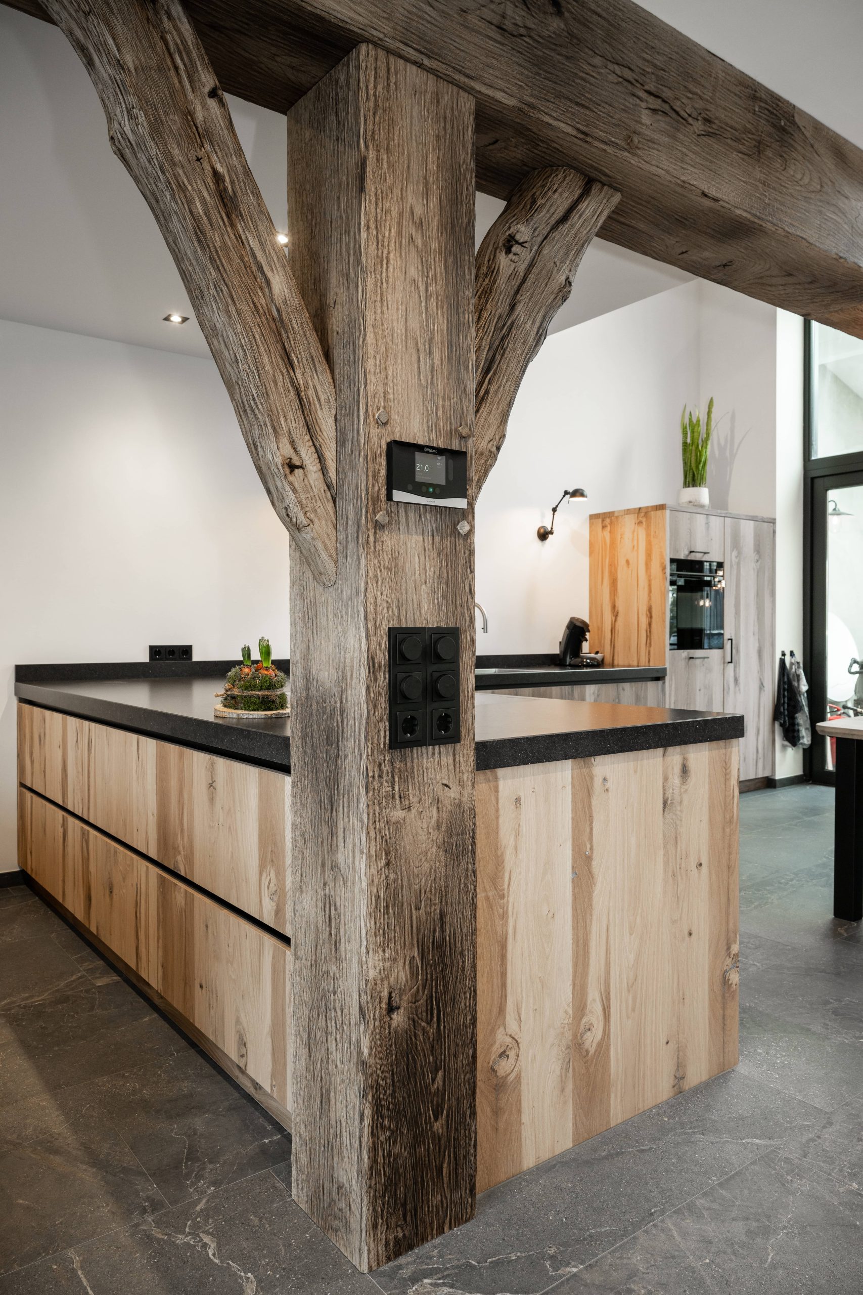 Stalen balk bekleden met barnwood: rustieke houten kolomafwerking in een interieur met een eikenhouten keukeneiland en natuurstenen vloer.